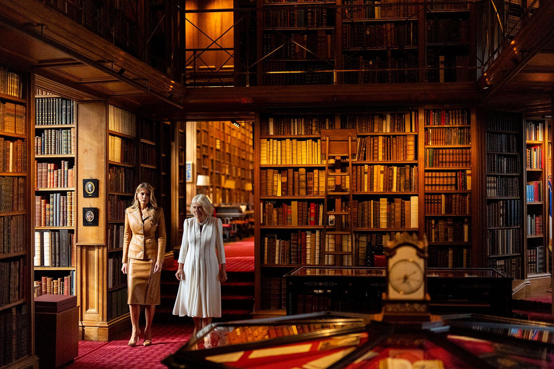 First Lady Melania Trump, wearing a light-brown leather two piece skirt suit, and Queen Camilla, wearing a mid-length white dress with blue stripes, walking through the Royal Library at Windsor Castle, Berkshire