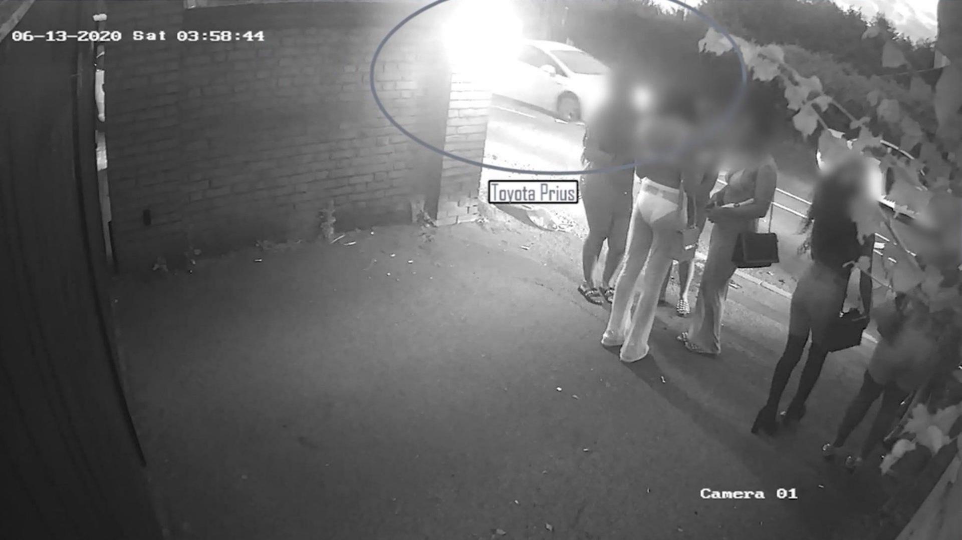 Young women standing in the dark as seen on CCTV. A Toyota Prius is highlighted driving past