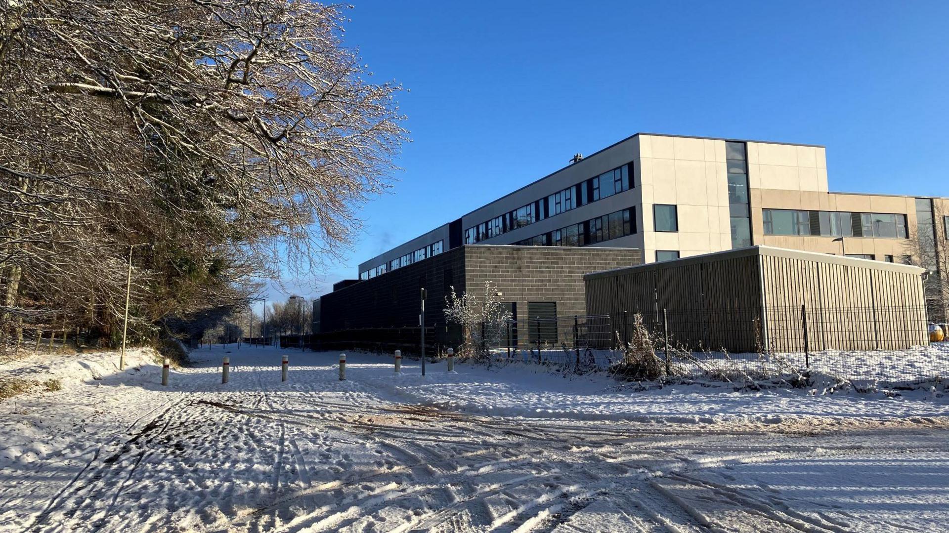 Inverness Royal Academy pictured on Thursday with snow on the ground. The sky is clear and blue. There is woodland on the right of the image.