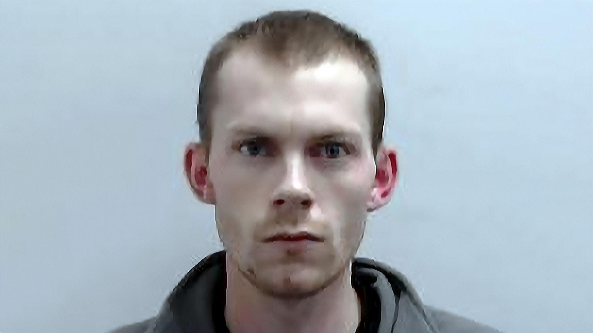 Close-up portrait of Connor Manners. He is facing the camera against a plain light background, with very short hair and wearing a grey top.