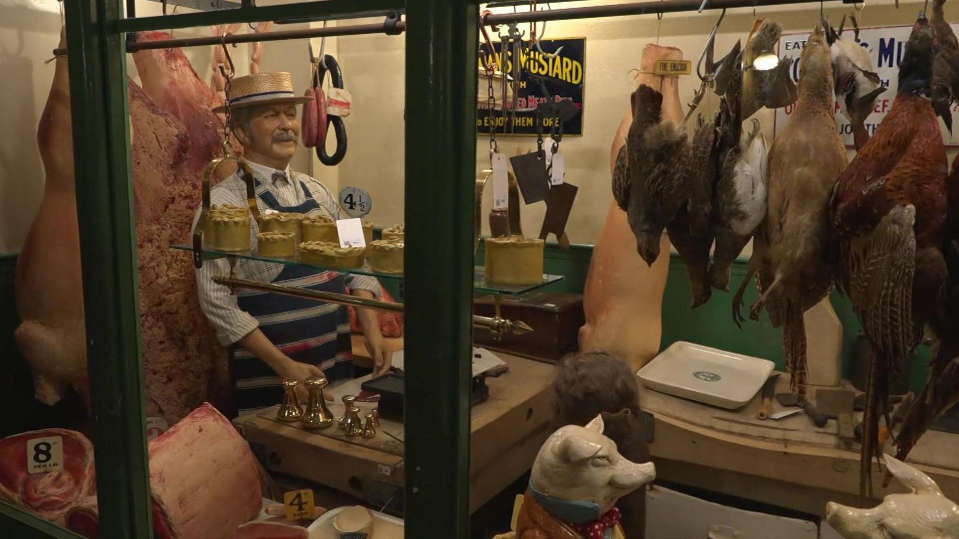 Mannequin of a shopkeeper inside a shop at the Victorian village. Fake poultry hang in the window. 