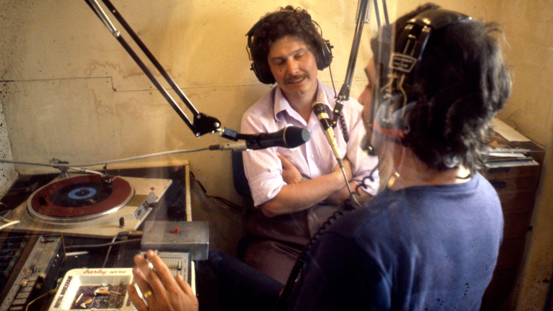 Dau berson yn darlledu, gydag un ohonyn nhw'n smocio