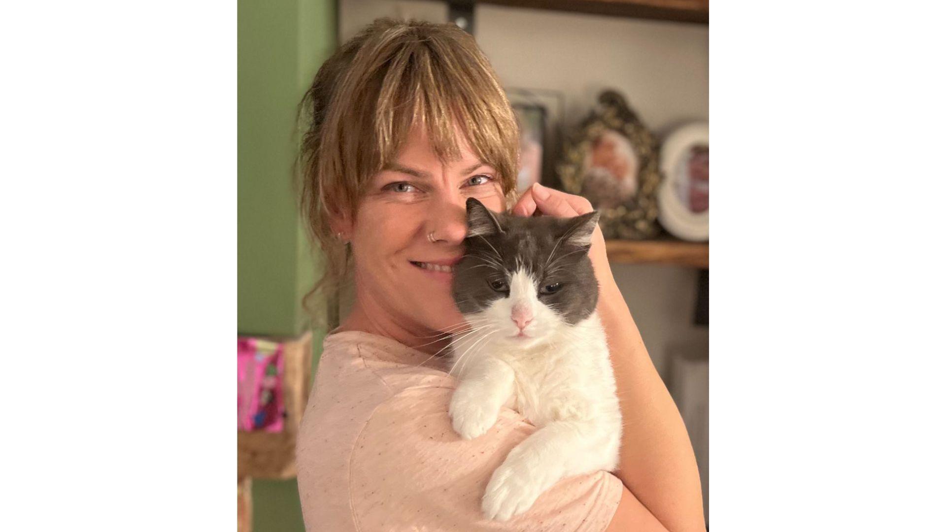 A smiling woman holds her mischievous cat who has been stealing cat food pouches from one of her neighbours.