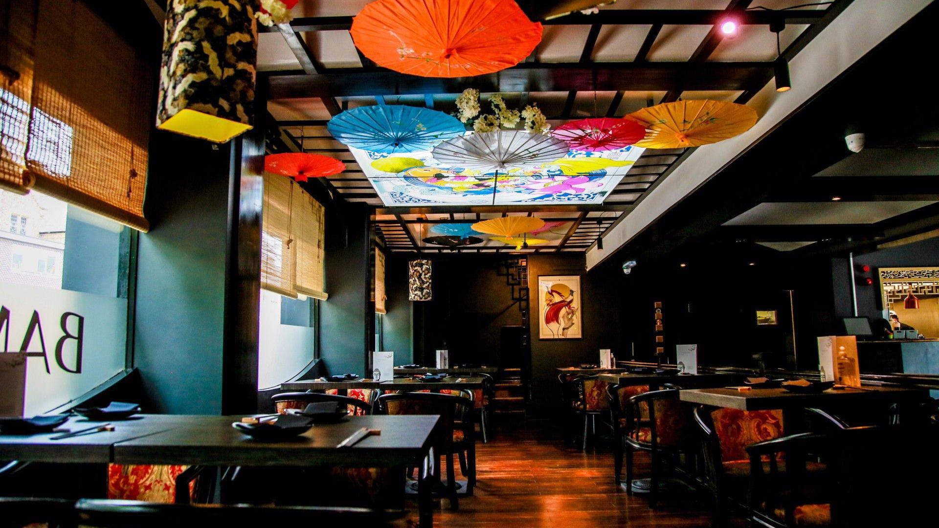 Inside of Bambudda restaurant in Darlington. It is an Asian restaurant and is decorated with black tables and chairs and has umbrellas hanging from the ceiling.