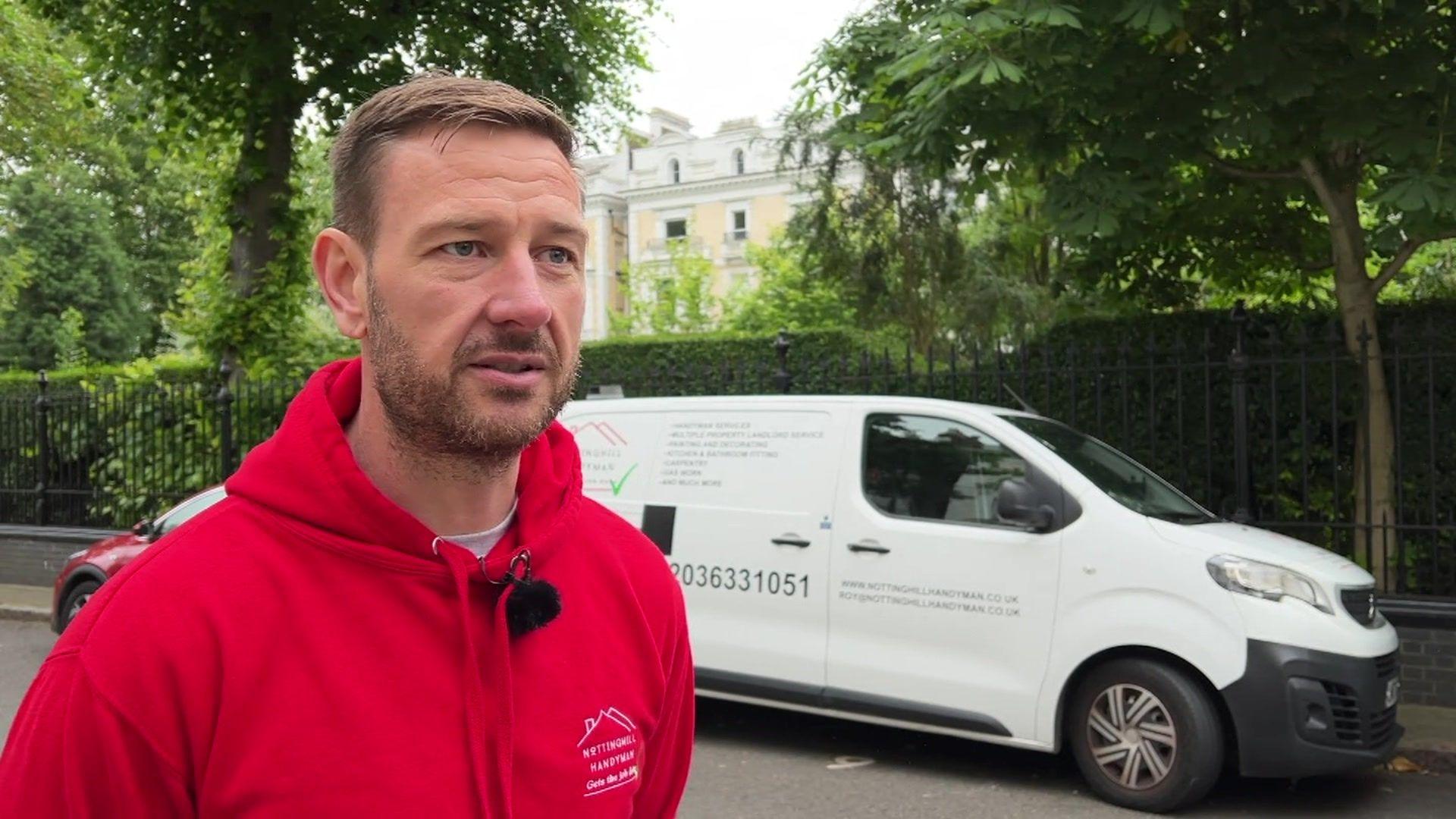 Roy Melville standing in a red hoodie in front of his van