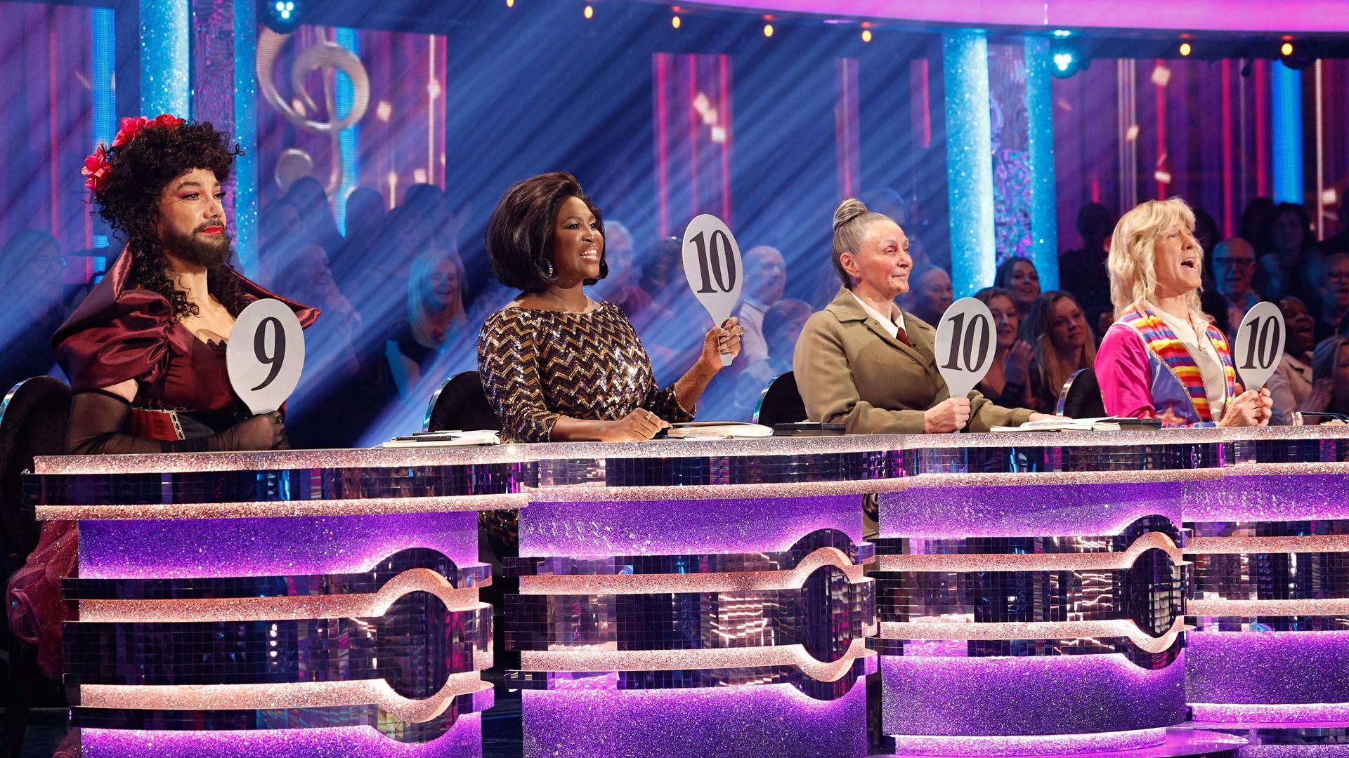 The judging panel at their desk in this year's Strictly Come Dancing. All the four judges - Revel Horwood, Motsi Mabuse, Shirley Ballas and Anton Du Beke - are in costume. Revel Horwood is holding up his scoring paddle that says "nine", while the others' say "10".