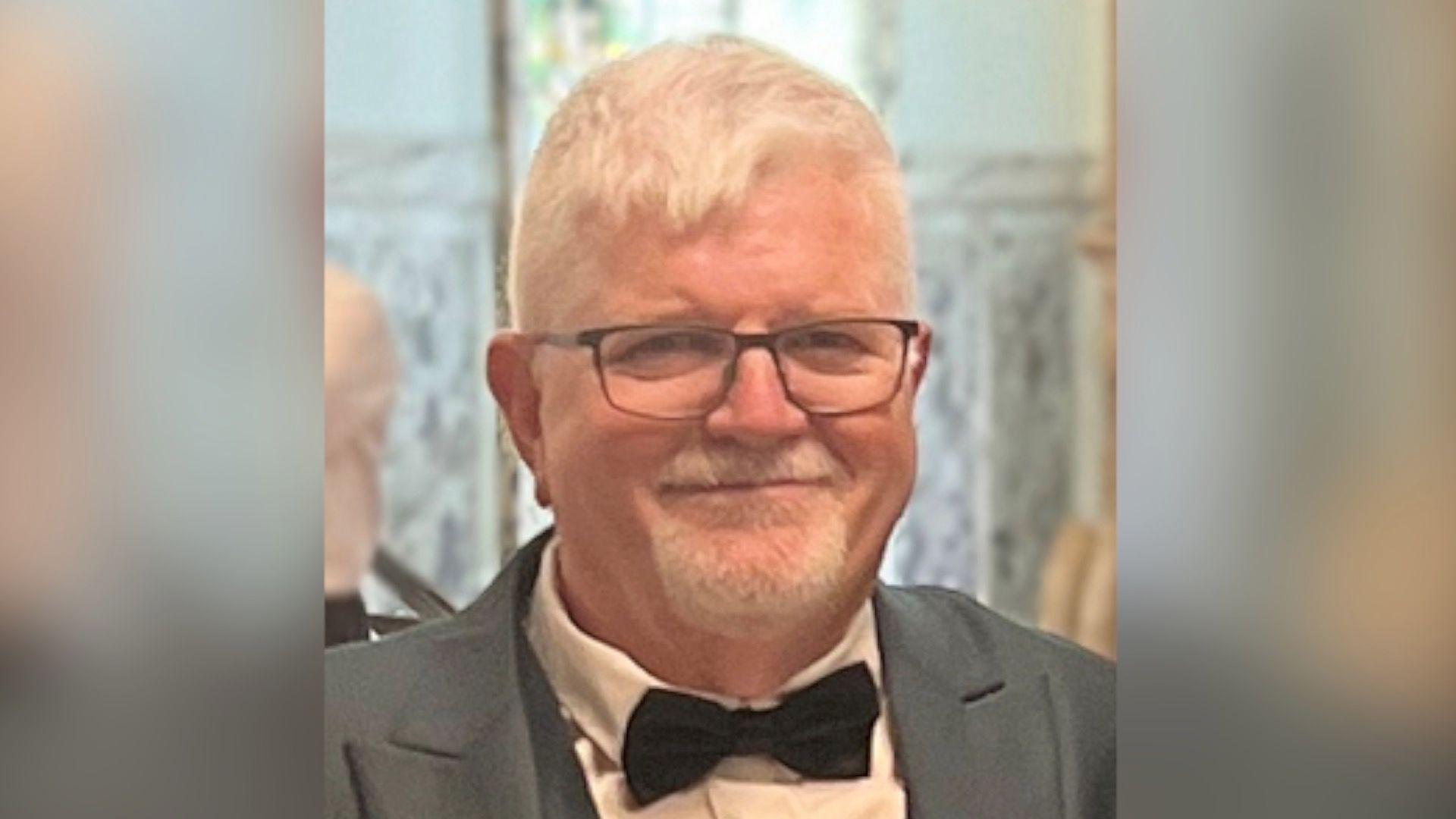 John Atkinson smiling. He is wearing a grey suit jacket, white shirt, black bow tie and black framed glasses.