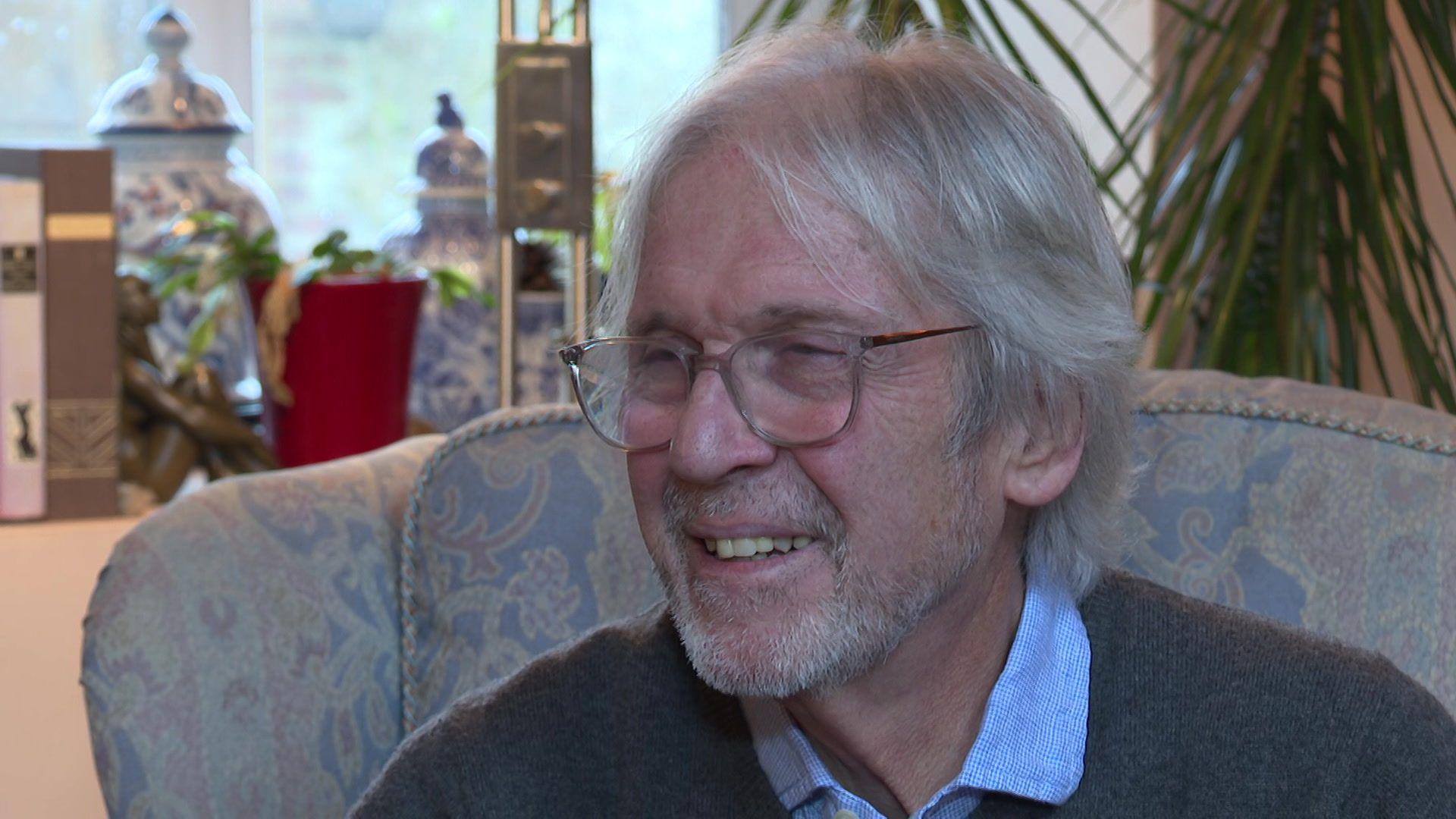 Iestyn Garlick yn gwenu ac yn gwisgo sbectol, siwmper llwyd a chrys glas.