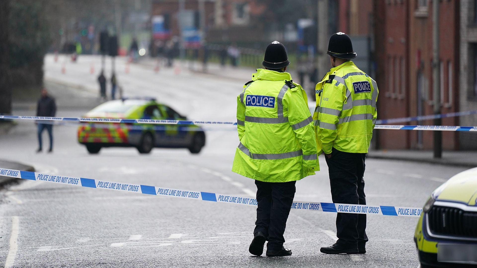 Two officers stand with their backs to the camera next to police tape with a police car in the road in the background in Leicester city centre on Wednesday morning.