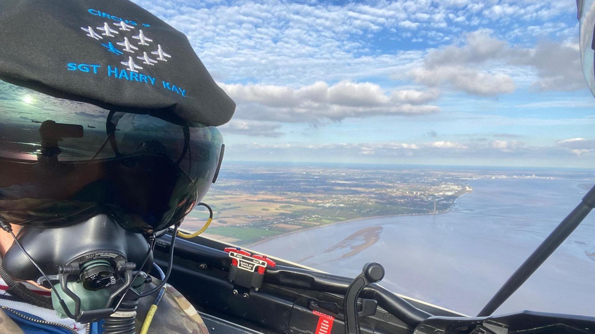 Sgt Harry Kay inside a jet flying over the Humber Estuary. He is wearing a helmet with his name and images of the nine Hawk jests marked on it.