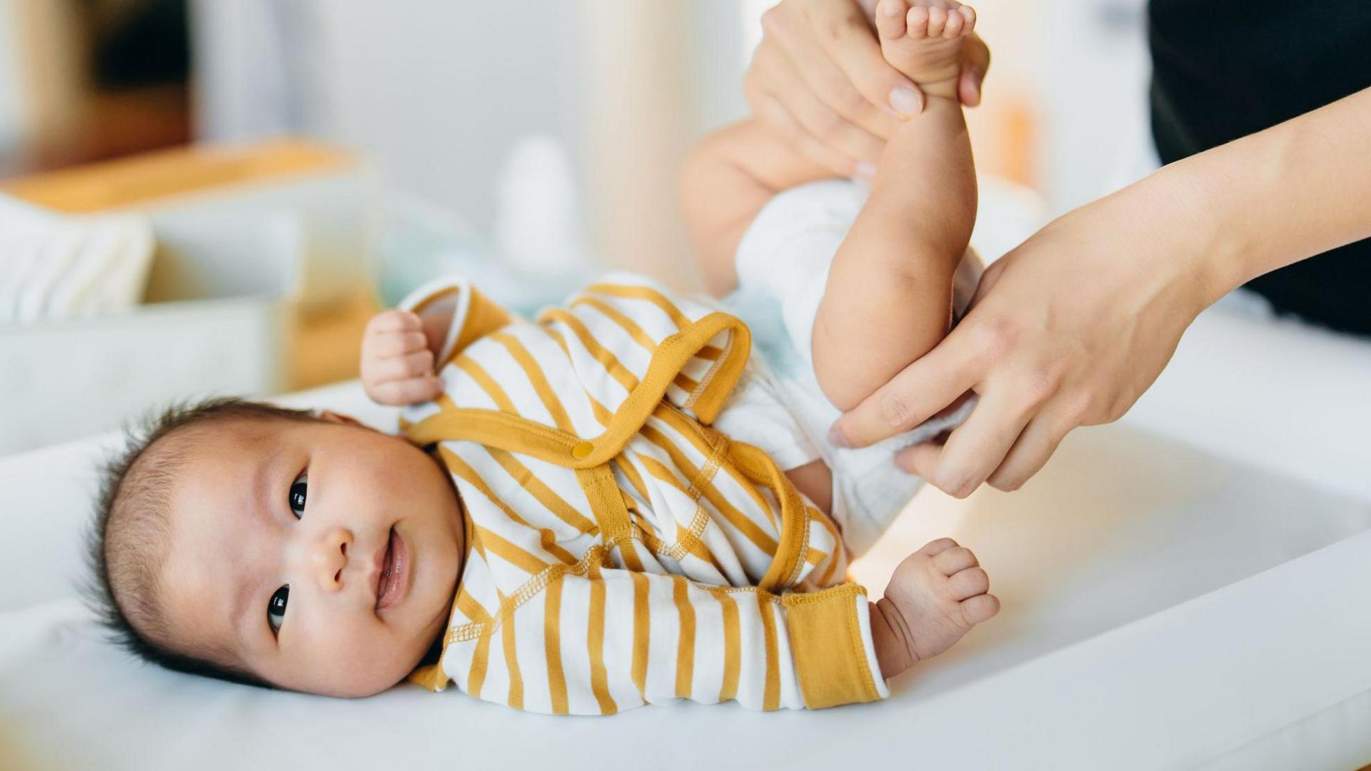 Baby in yellow/white striped vest smiling through a nappy change