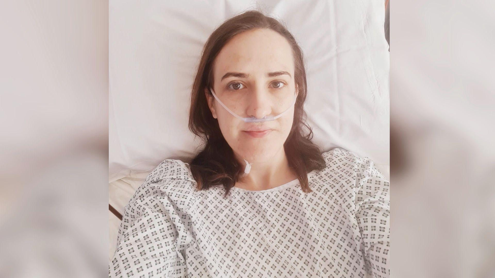 Rachel Davies wearing a hospital gown and lying in a bed.