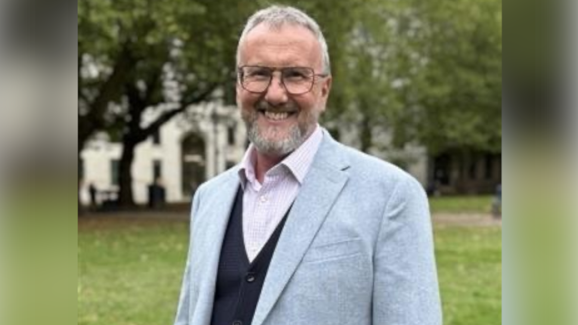 Steve Milburn, a man who is standing outside and looking directly at the camera and smiling. He is wearing a grey suit jacket and pink shirt.