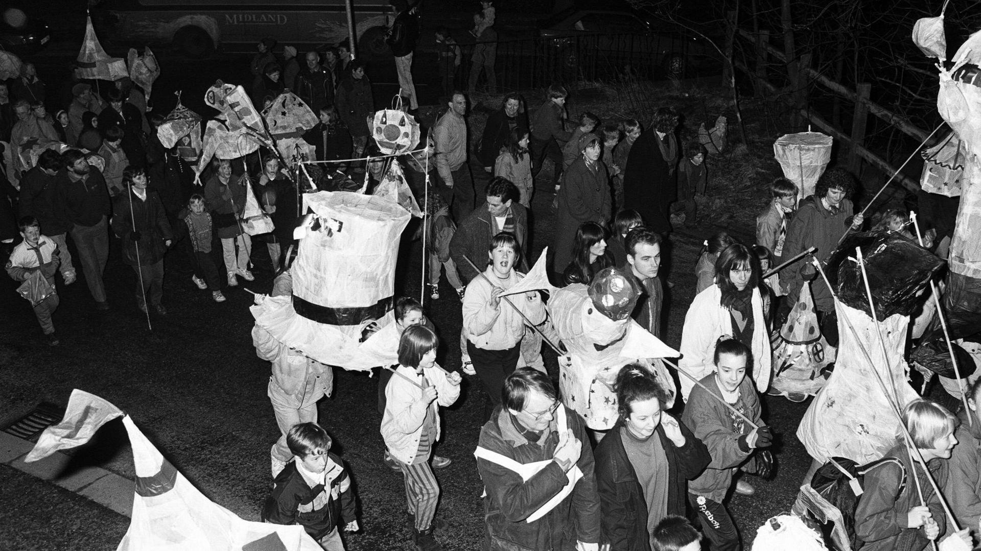 A black-and-white photograph of people parading through Slaithwaite with homemade lanterns in the 1990s