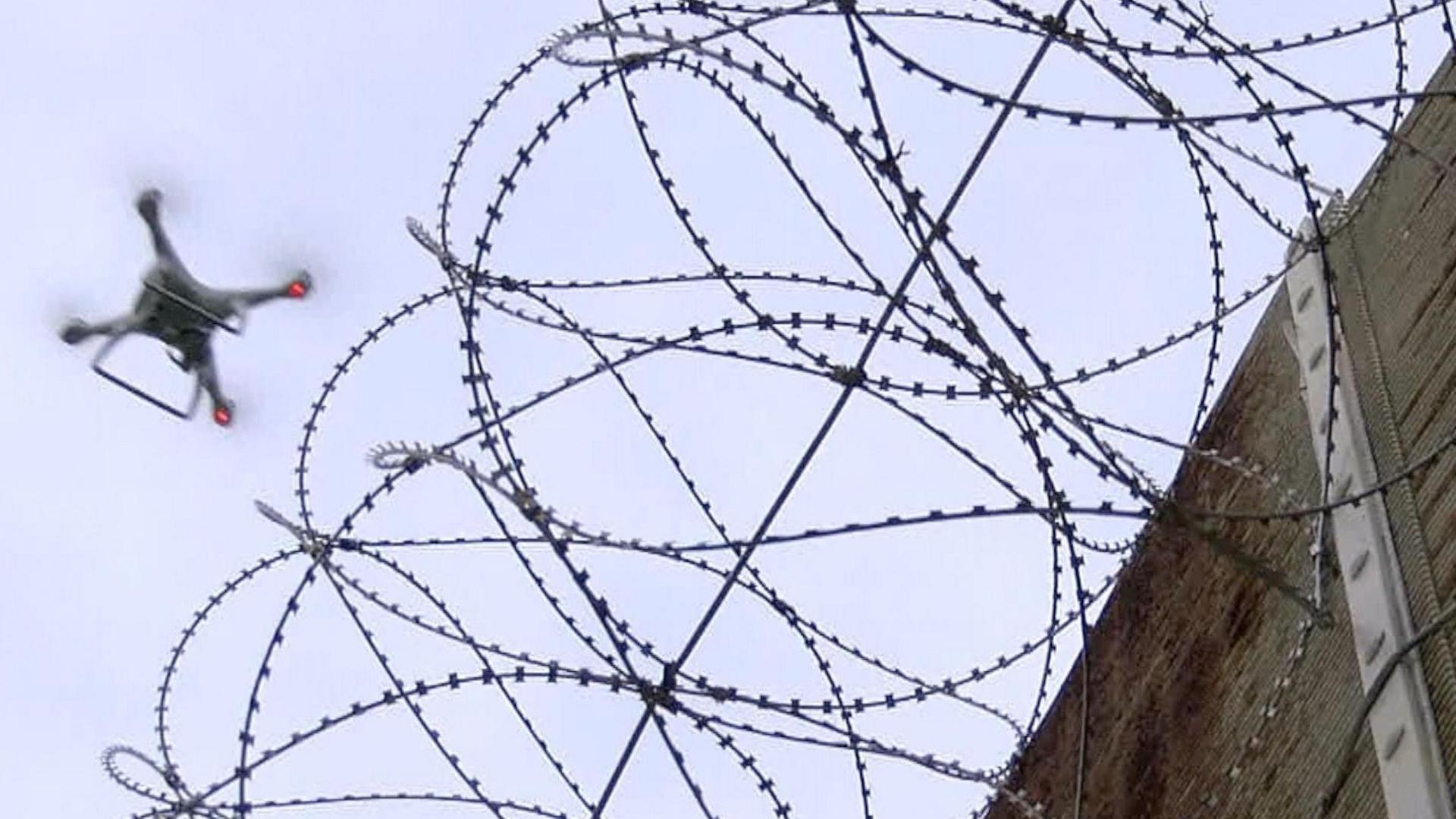 A picture of a drone, which has four arms with rotors attached, flying next to a wall toped with curls of barbed wire