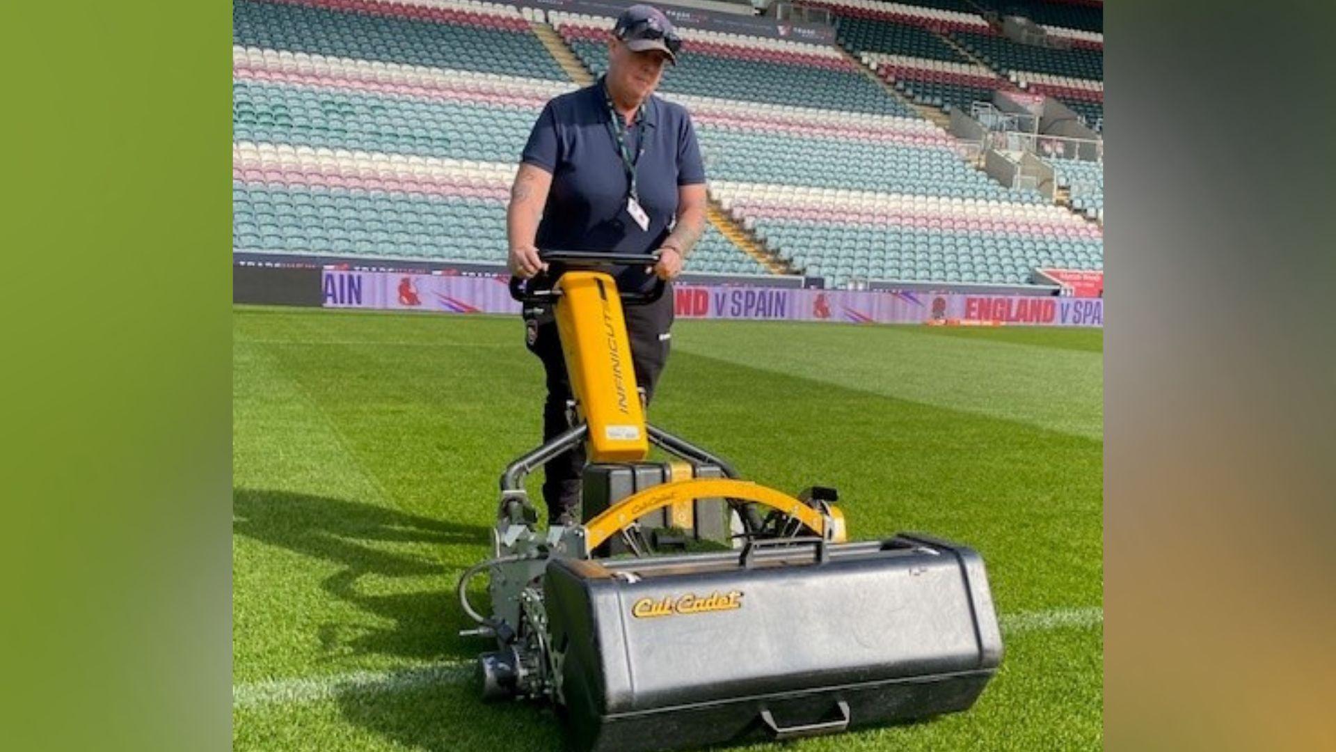 A woman using a lawnmower on a rugby stadium pitch