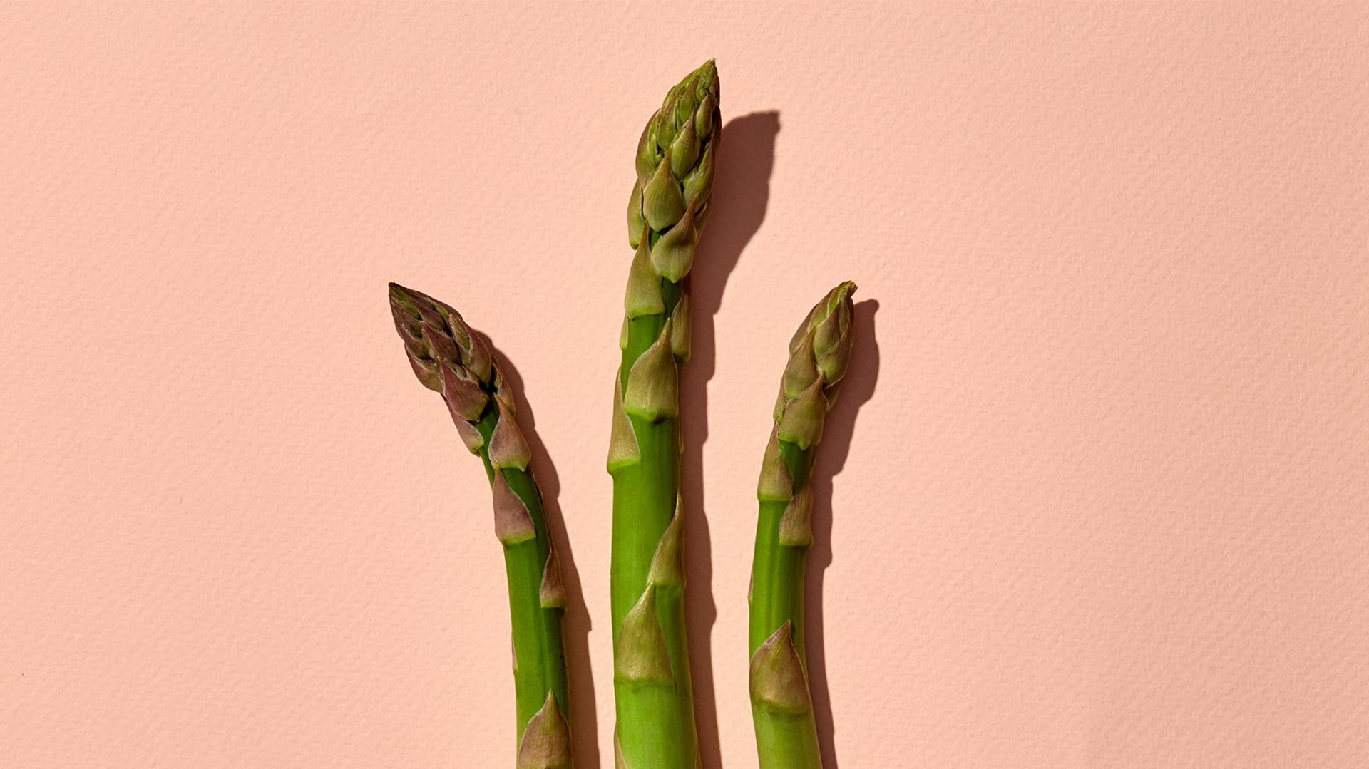 Three asparagus spear tips on a pink background