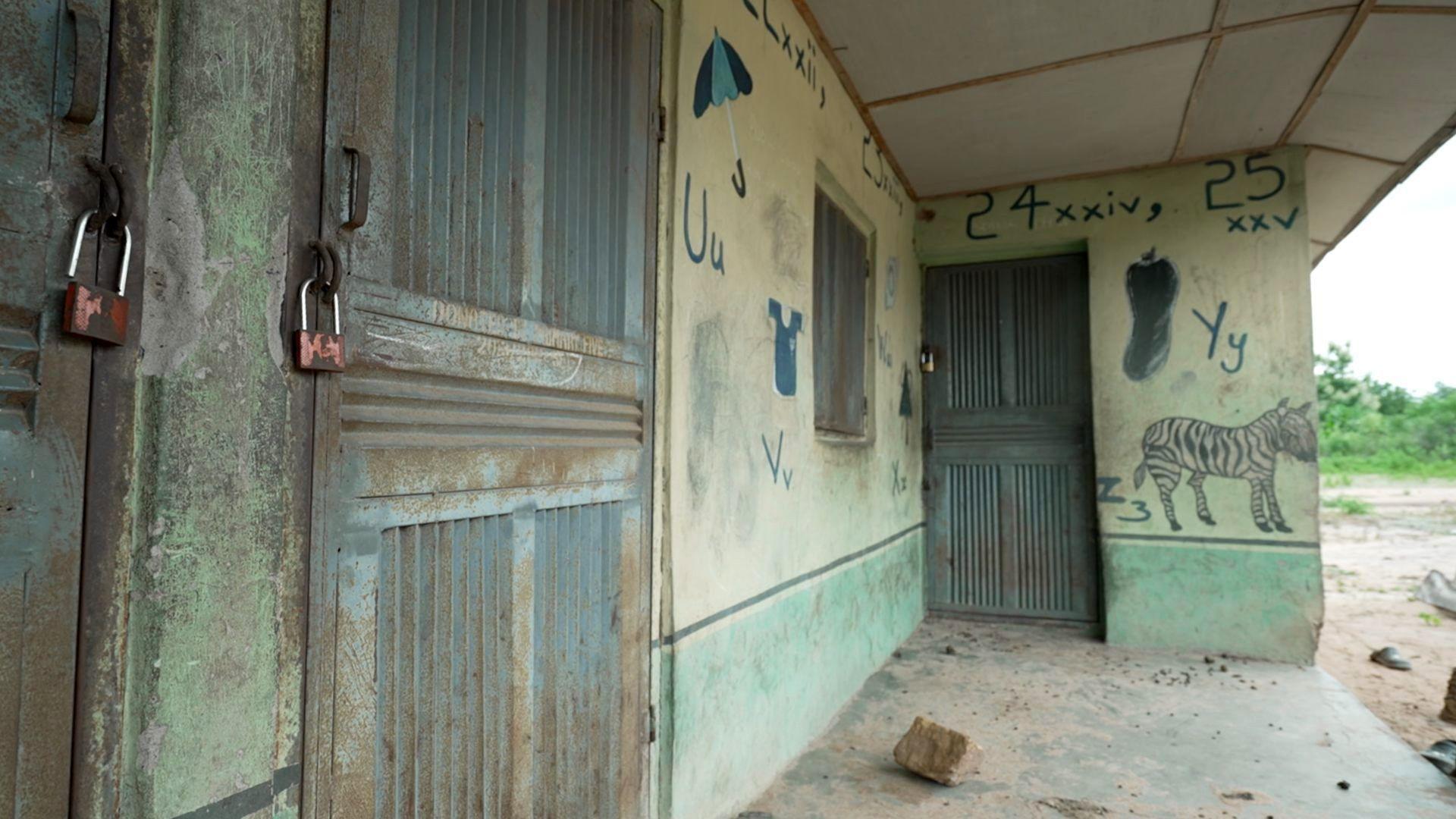 The beforehand of a schoolhouse building, the doors unopen and padlocked. Children's drawings, included 1 of a zebra, decorate the walls