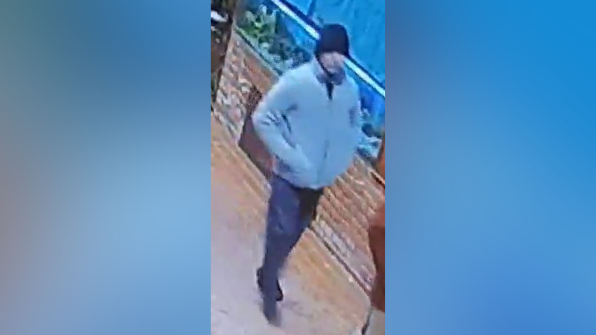 Daniel Washbourne po ecën nëpër një rrugë, i veshur me një kostum leshi ngjyrë krem, tuta sportive blu, kapelë blu dhe atlete të zeza.