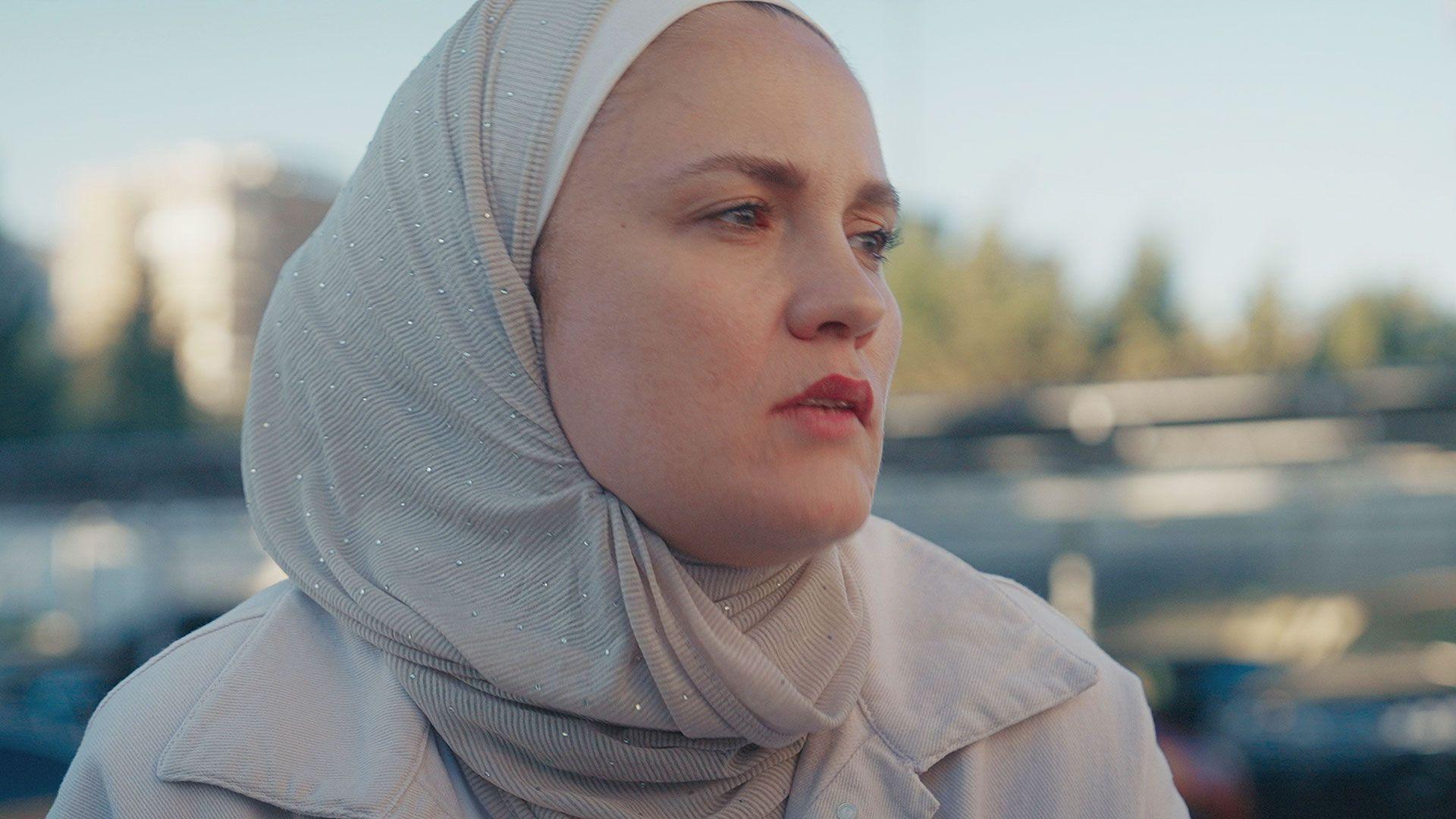Reem is wearing a soft grey headscarf and a light coat and is looking into the middle distance