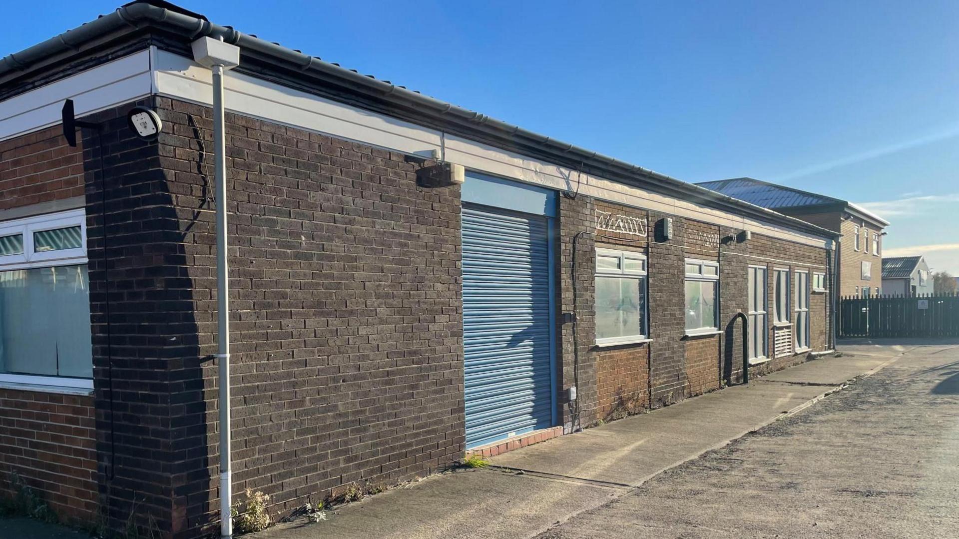 An empty industrial unit with blue shutters pulled down.