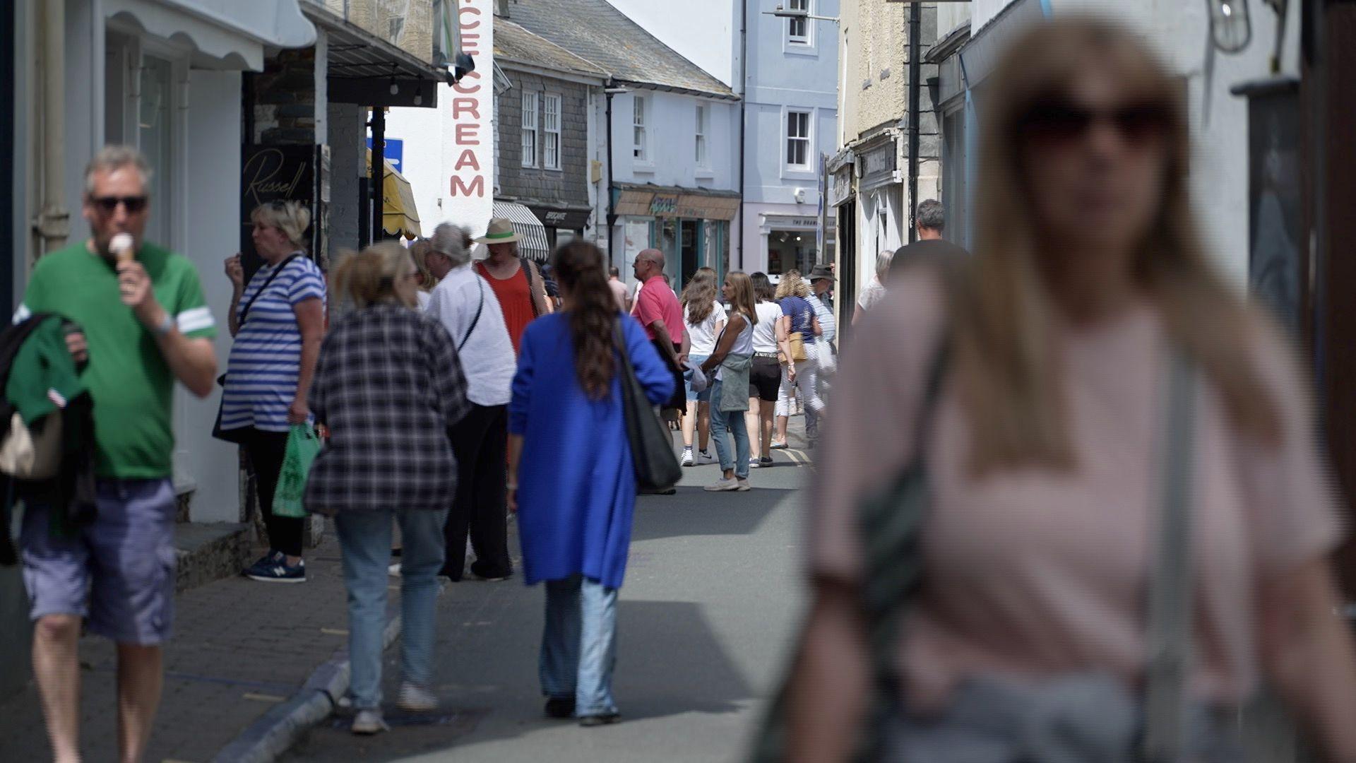 View down a busy street with people walking and one person eating an ice cream  