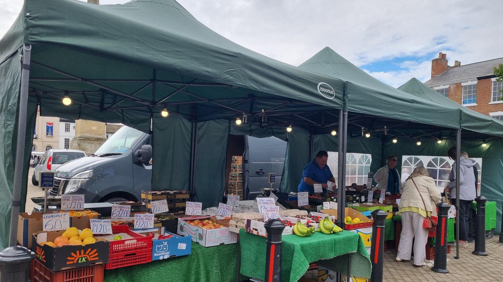 A large green gazebo erected in Ripon market with a large display of vegetables on tables underneath
