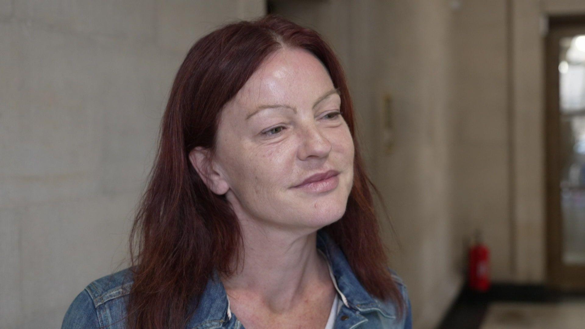 Councillor Christine Townsend wearing a blue denim jacket and standing in the hallway of a white stone building. She has dark red-brown hair and thin eyebrows, and is looking off to the right of the camera.