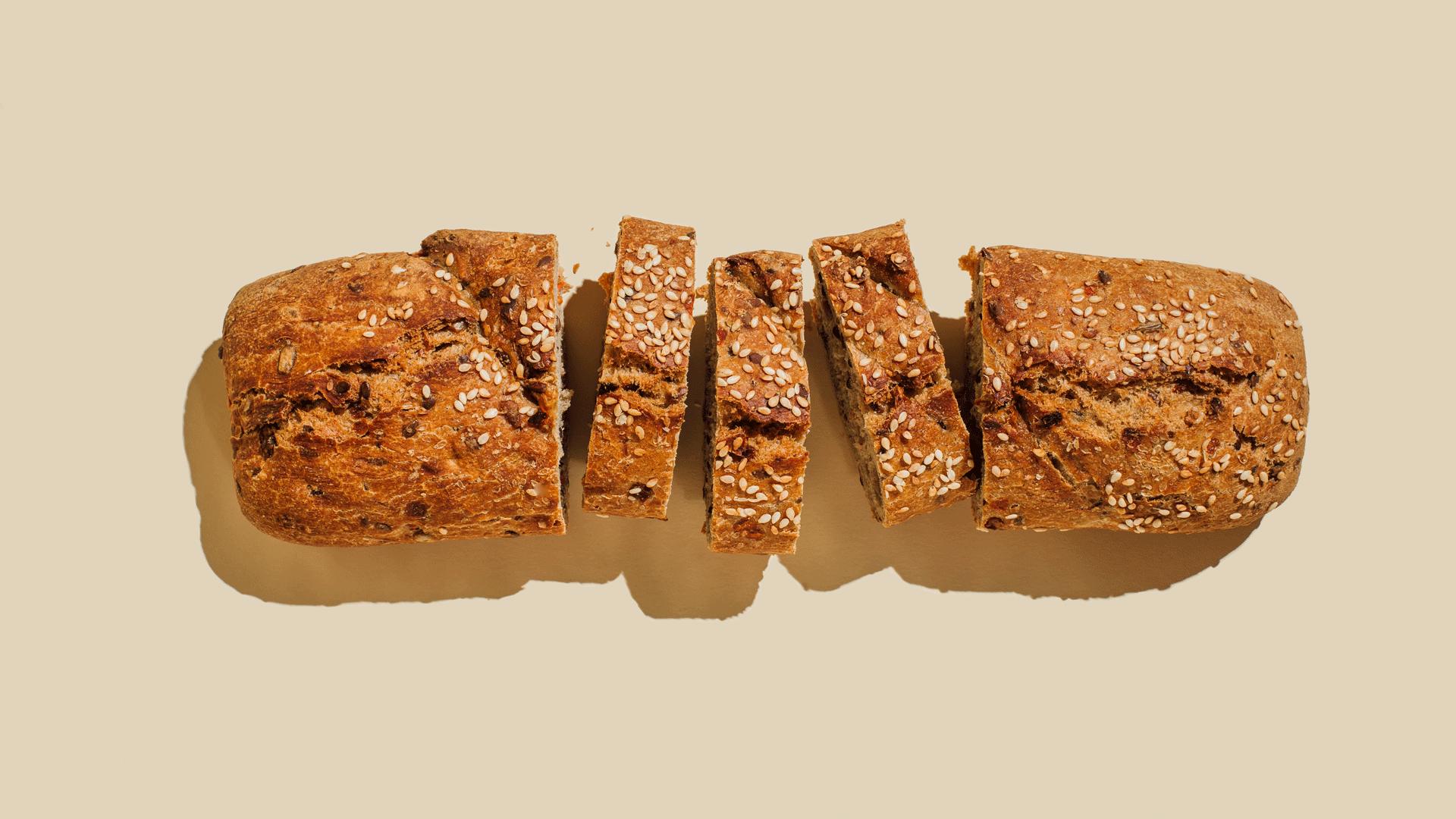 Loaf of wholemeal and seeded bread. Three slices in the middle have been cut. The bread has a shadow coming off it and it's on a pale beige background. 