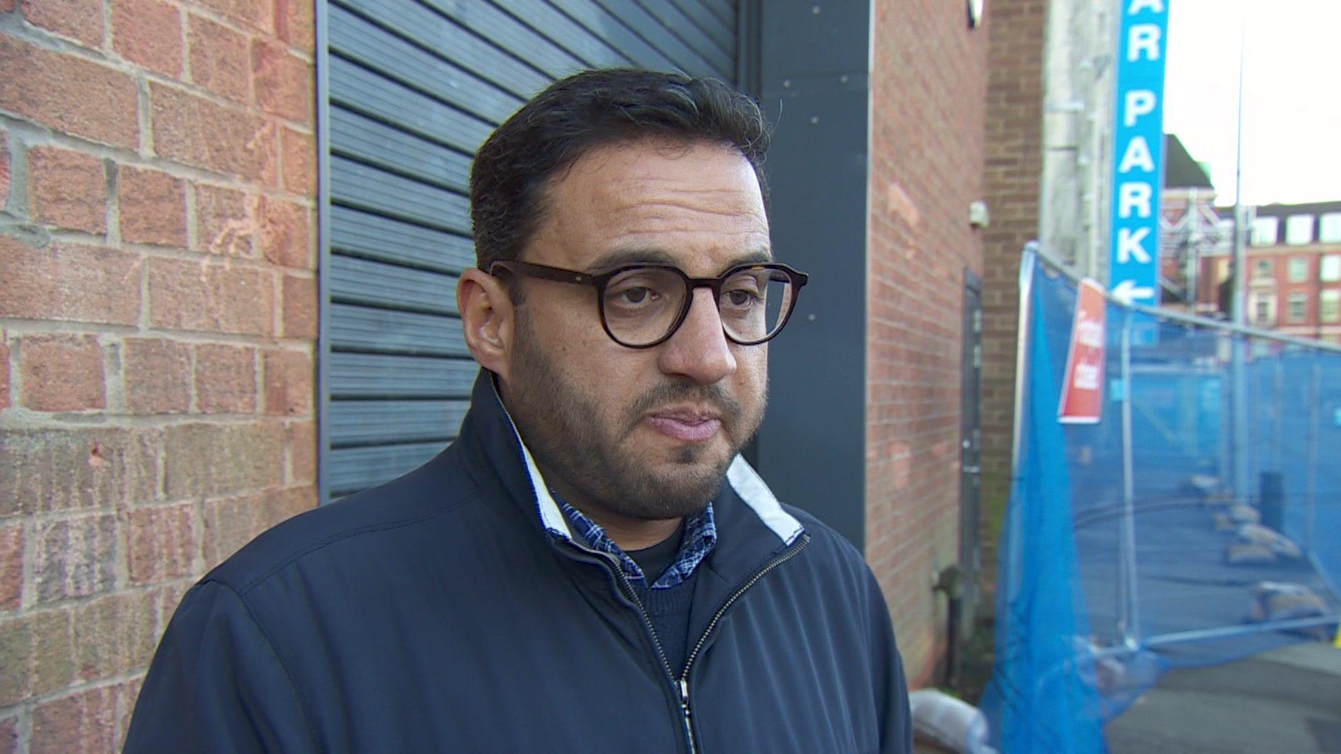 Mohamed standing in the street wearing a blue jacket. He is wearing glasses and has dark hair and short beard.