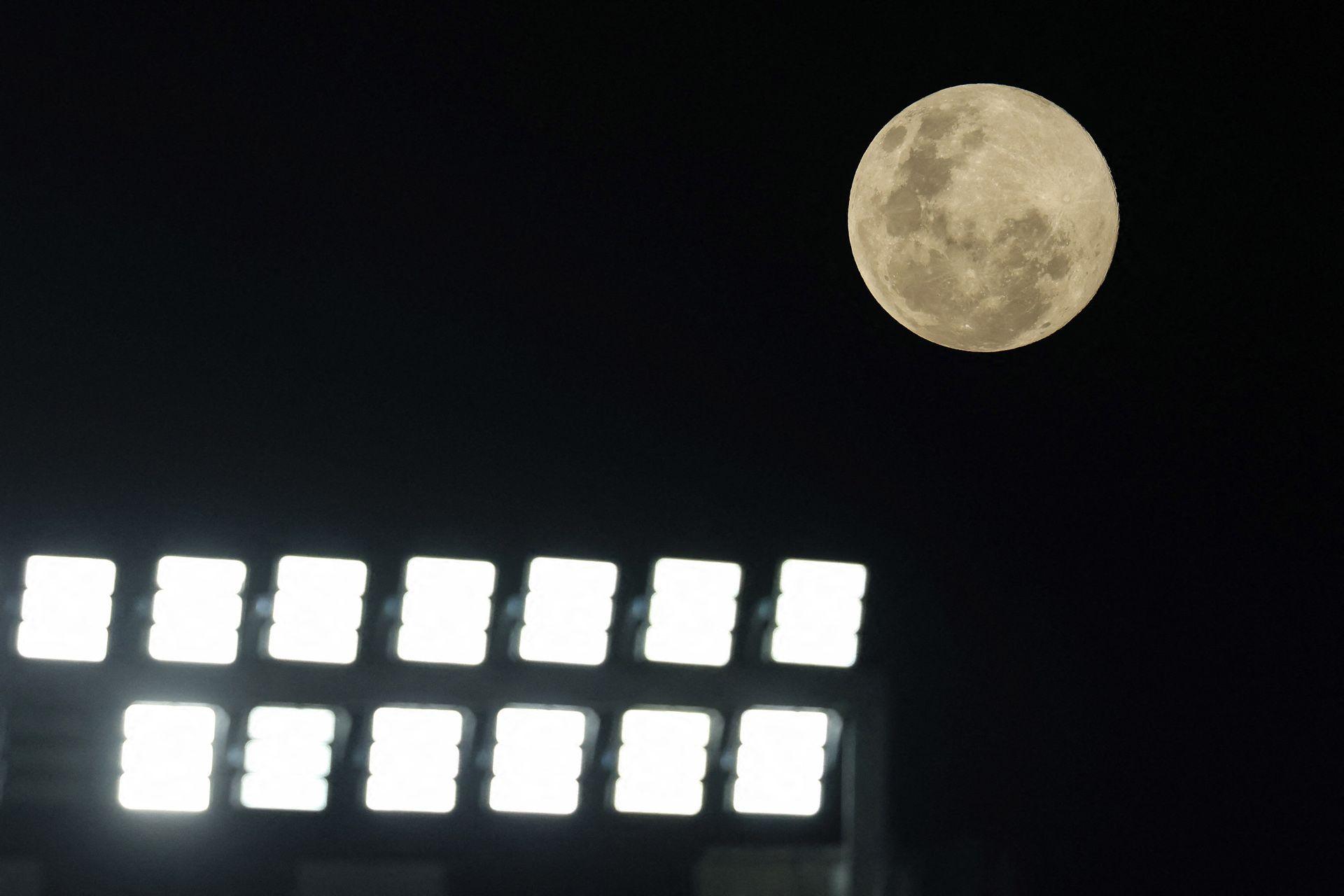 The Moon is seen clearly on the right of frame against a dark starless sky, while floodlights glare in the foreground, in Auckland on Wednesday.