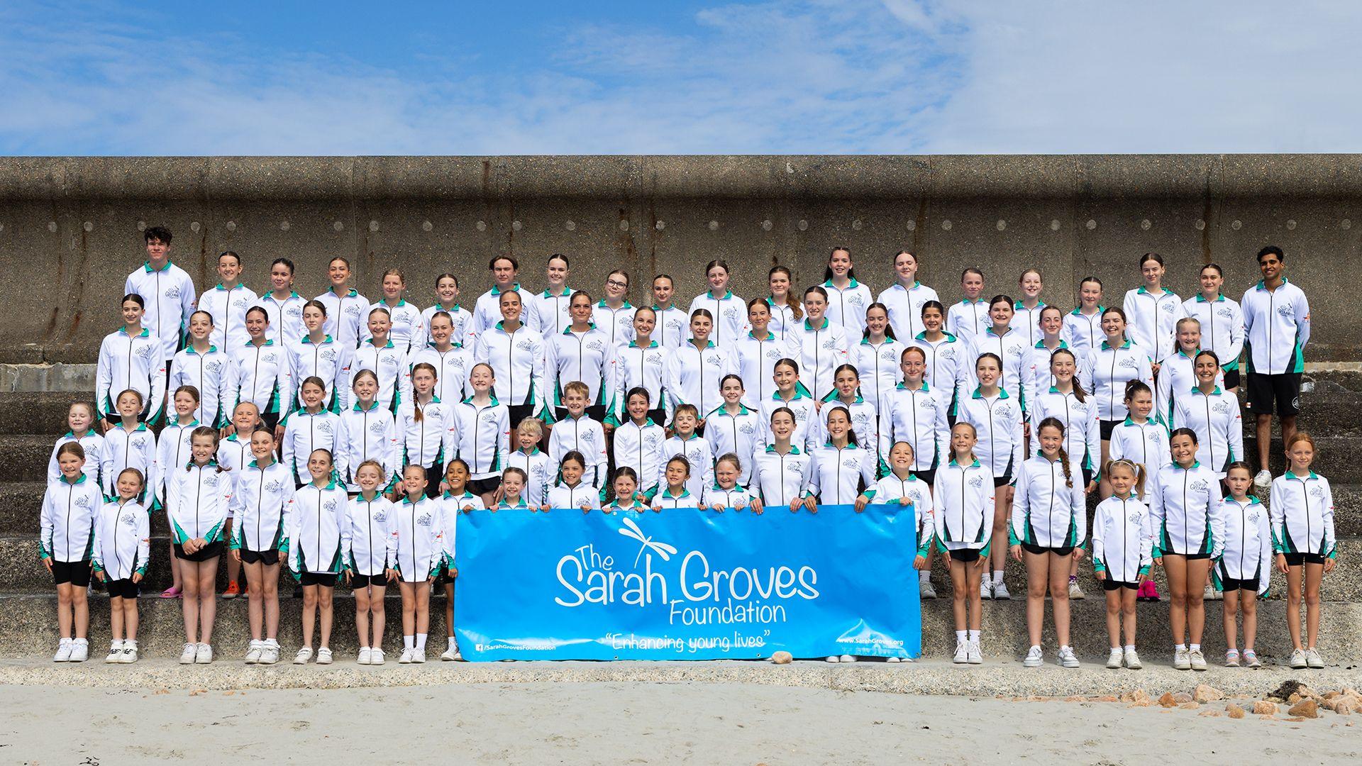 A group of young dancers standing with a Sarah Groves Foundation banner. 