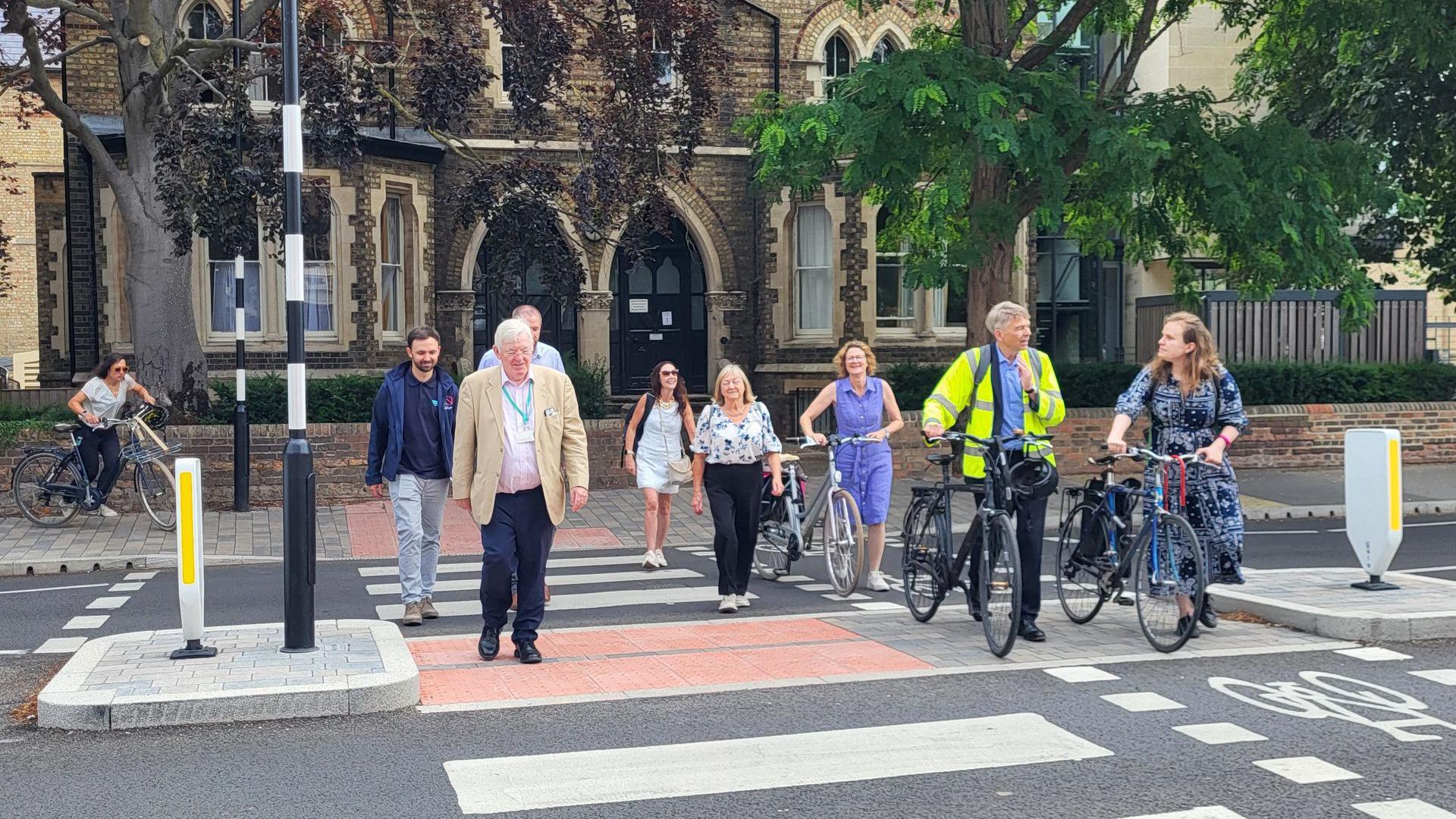 From left to right a group of people walk across a zebra crossing - Valerie Lambrechts, Joe Bates, Patrick Mulvihill, Craig Buzzard, Helen Fallon, and Councillors Judy Roberts, Louise Upton, Andrew Gant and Emma Garnett