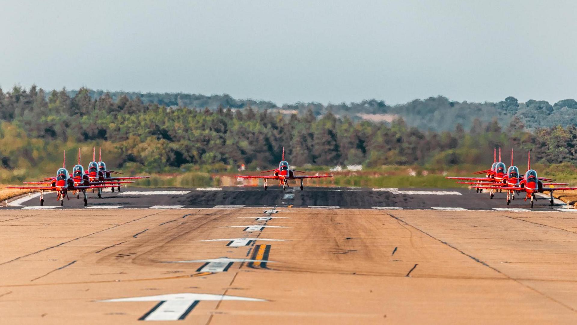 The Red Arrows lined up on an airport runway.