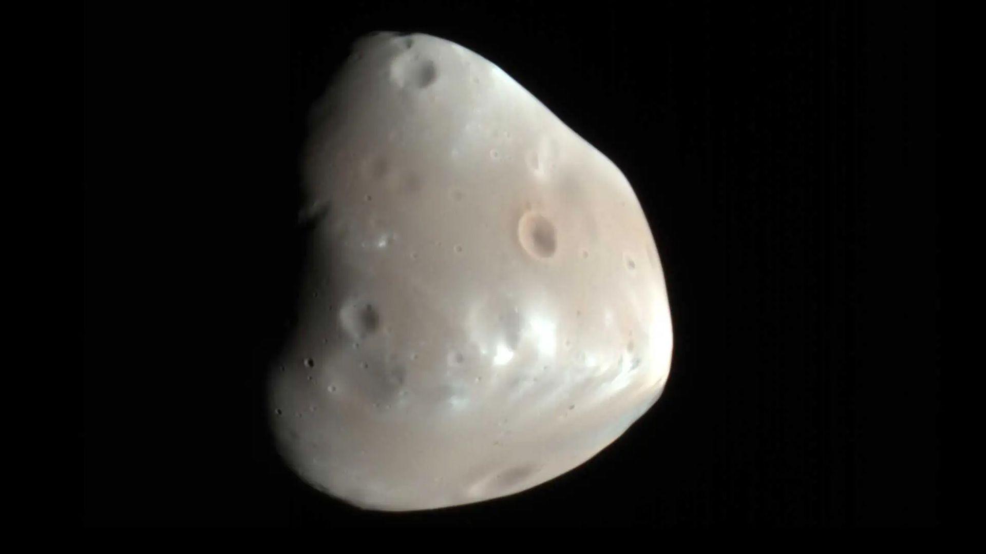 The moon of Deimos - a white, lumpy rock shape with small craters - on the black background of space