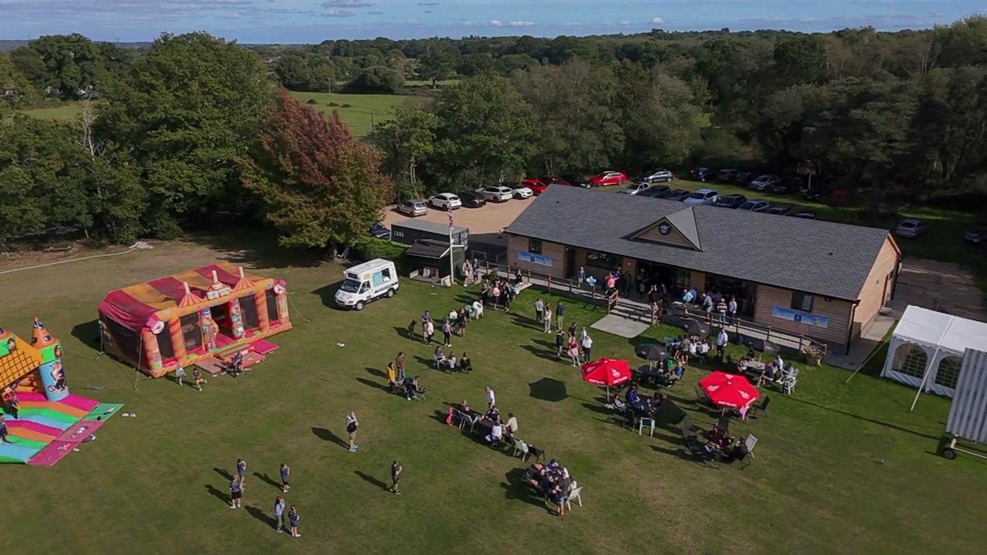 An aerial shot of the new cricket pavilion being opened with crowds of people and bouncy castles on the cricket green