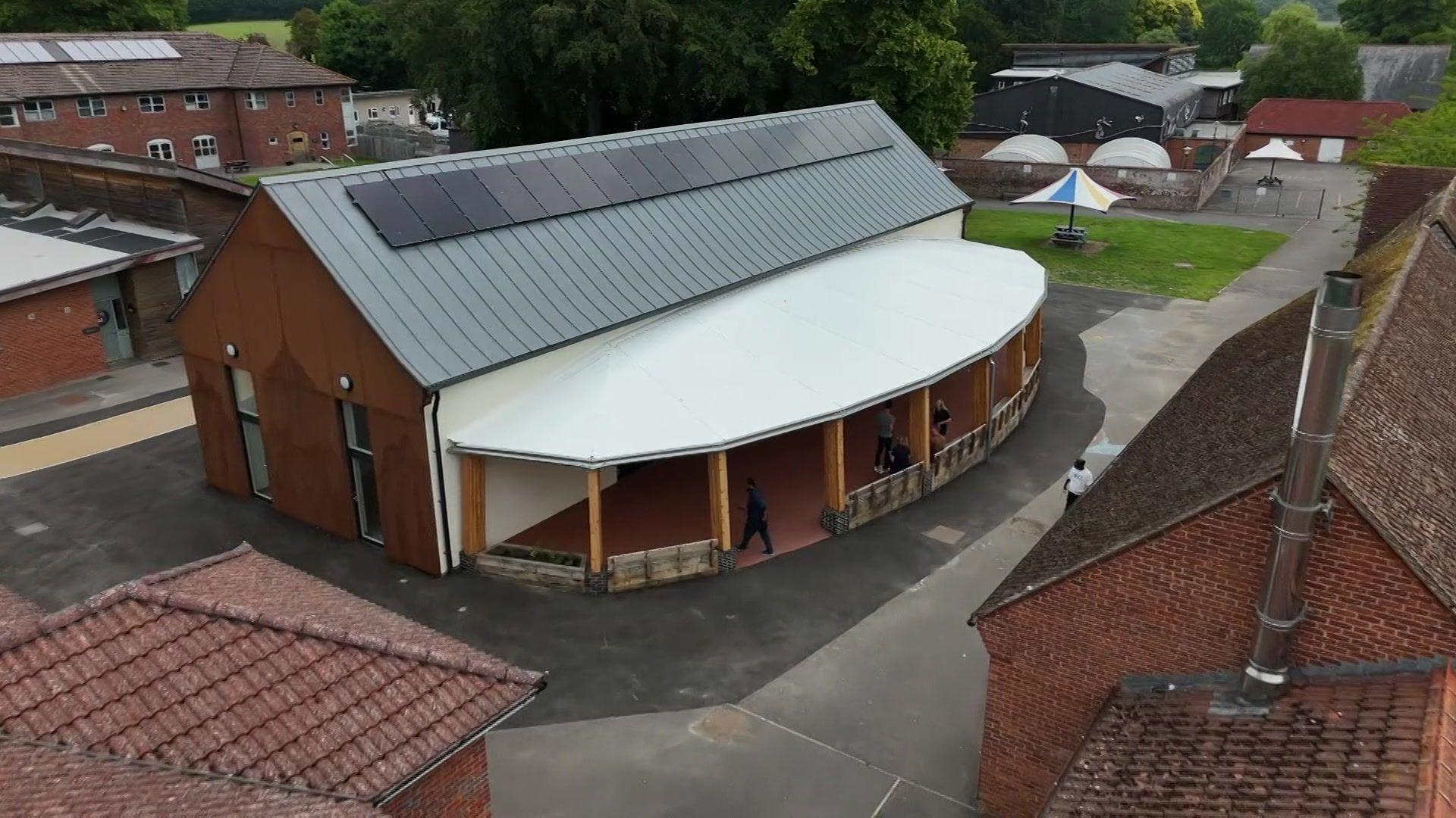 A large wooden building sits between older red brick buildings.