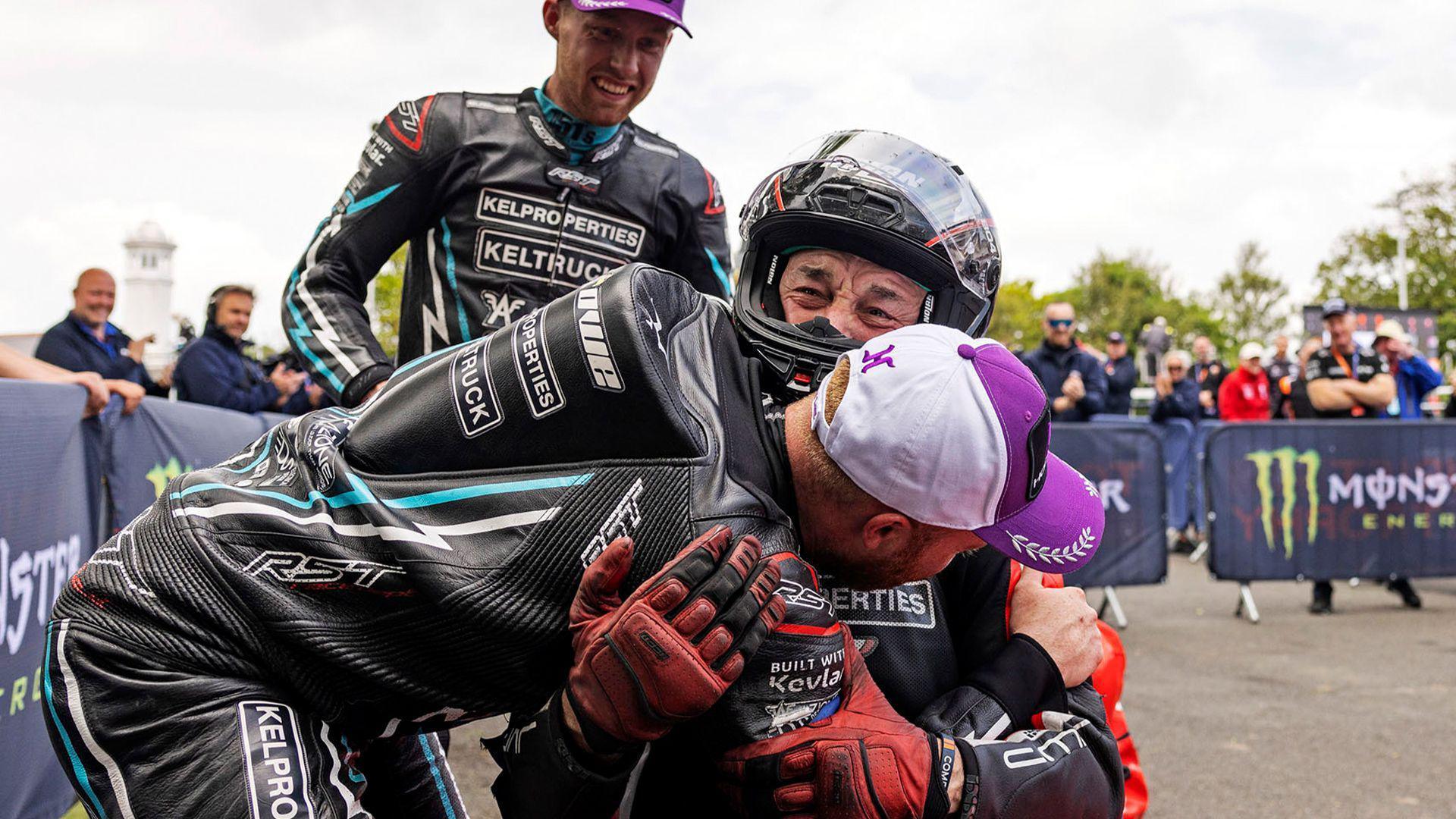 A sidecar crew in black leathers congratulating a man sitting in a red sidecar outfit