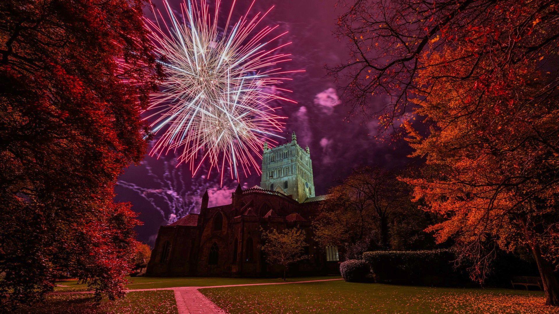 Fireworks in front of Tewkesbury Abbey with orange and pink colours surrounding it.