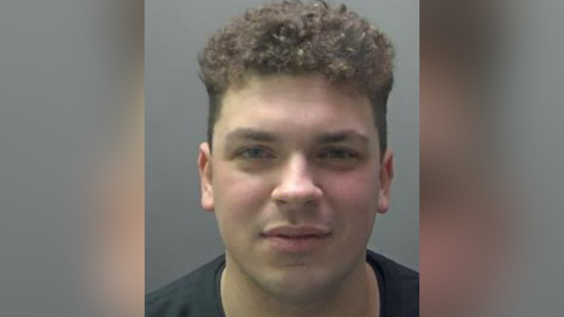A police image of Jake Cummings: The head and shoulders of a man with dark, curly, hair wearing a black, round-necked top.