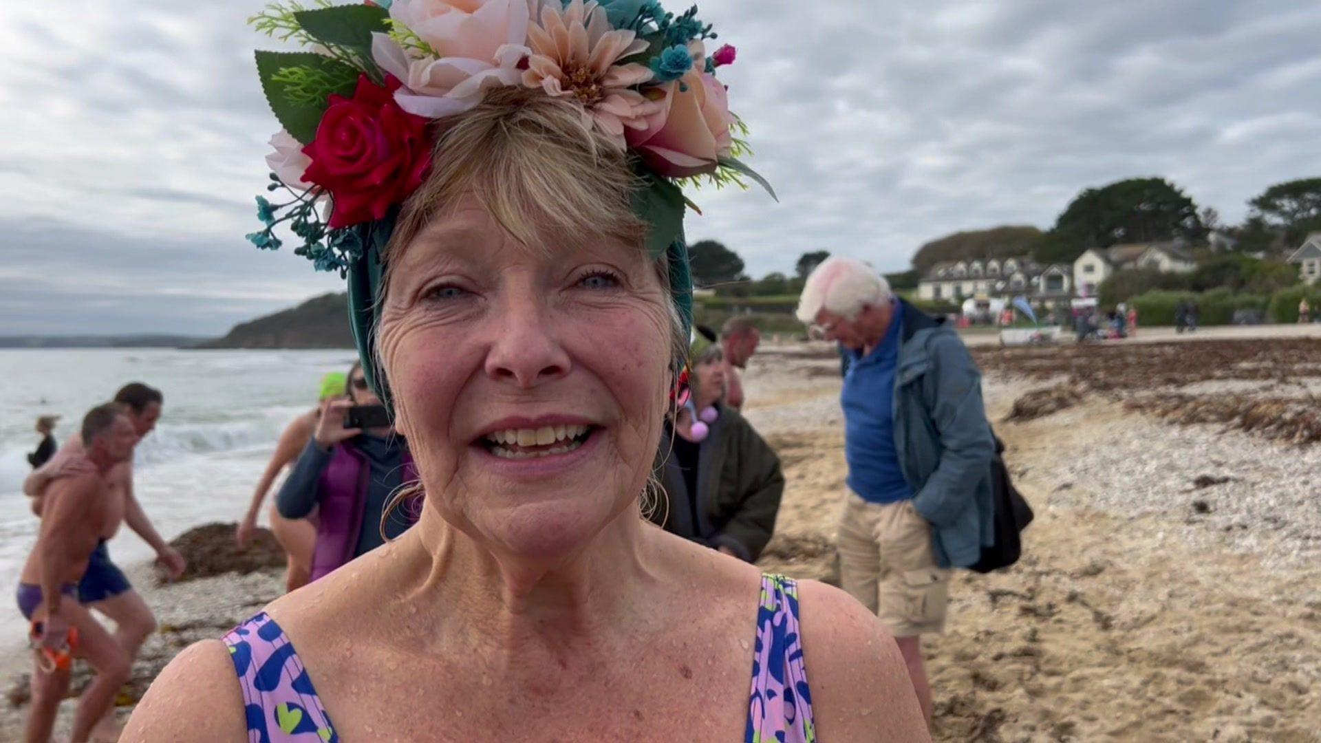 Ruth Hitchcock, standing on a beach with flowers in her hair and wearing a blue, green and pink swimsuit, after completing her 365th swim