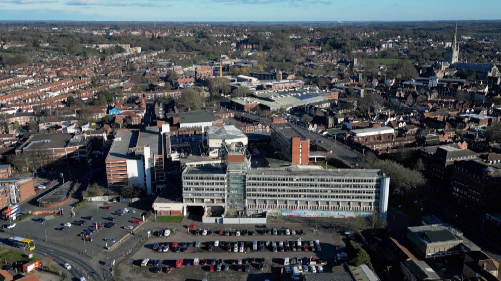 Aerial view of Anglia Square and part of the city of Norwich.  Car parks can be seen and a large concrete building is in the forefront of the image.