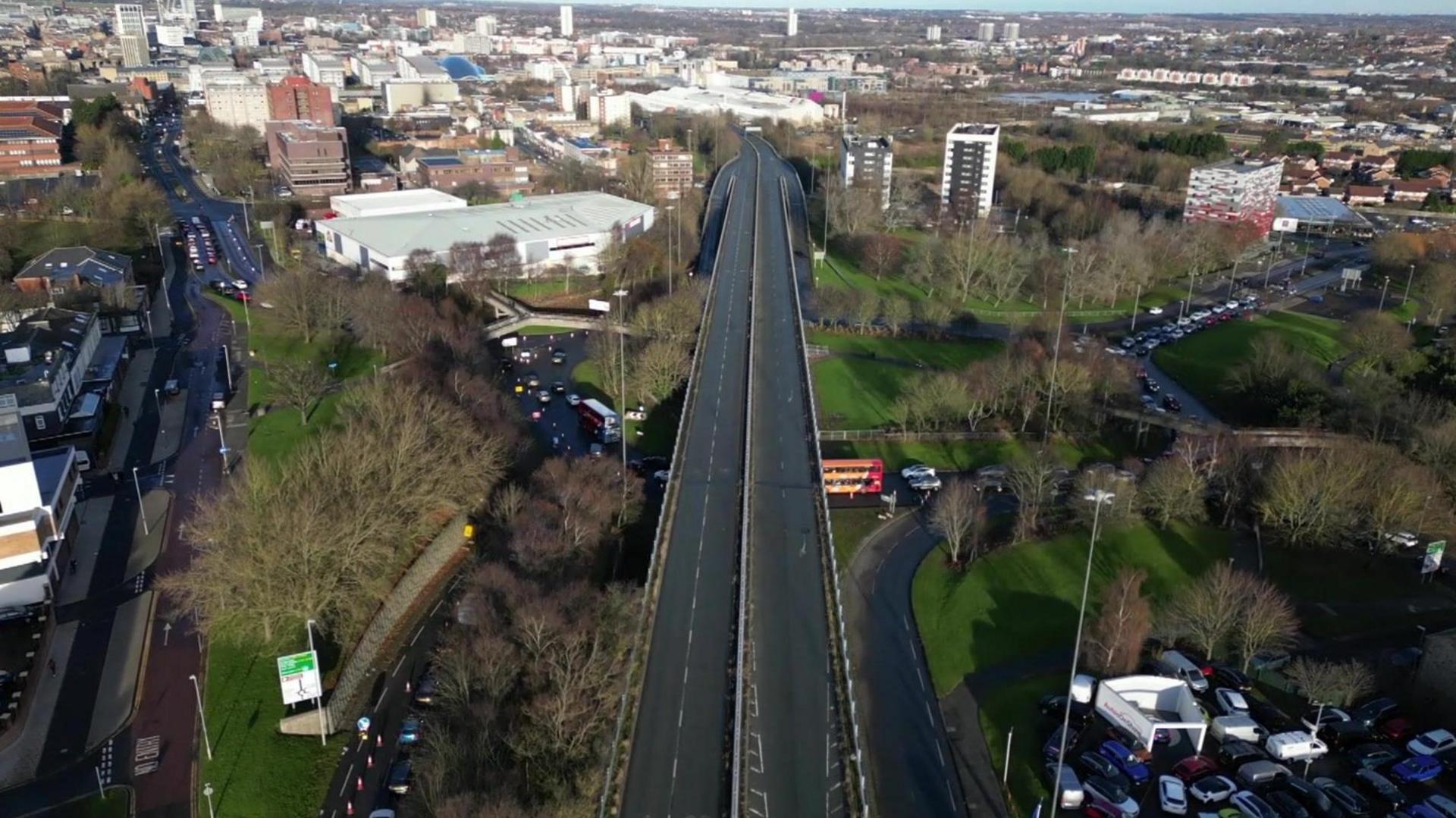 An aerial view of the flyover which is a dual carriageway above roads and trees.