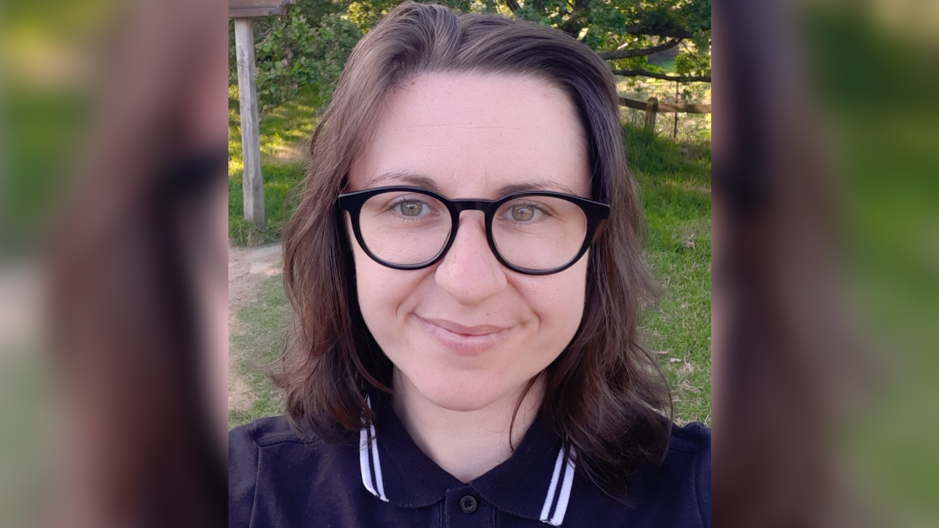 A woman with brown hair and glasses, wearing a polo shirt, smiles at the camera in a selfie.