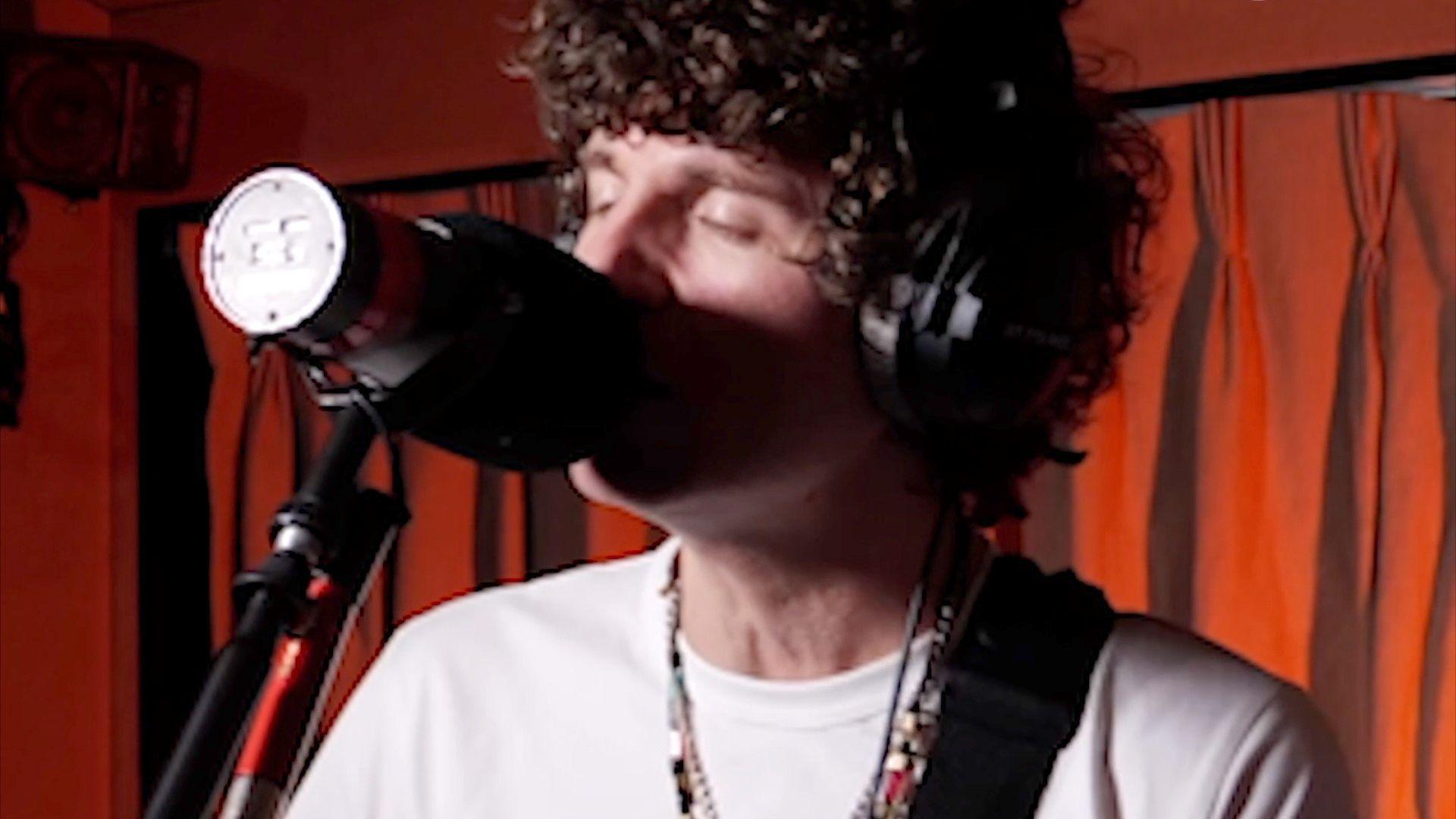 Luke Pritchard wears headphones and sings into a microphone