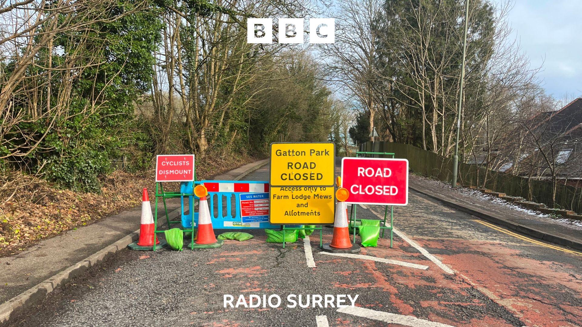 A single carriageway road is blocked by blue plastic fencing and a large road closed sign.