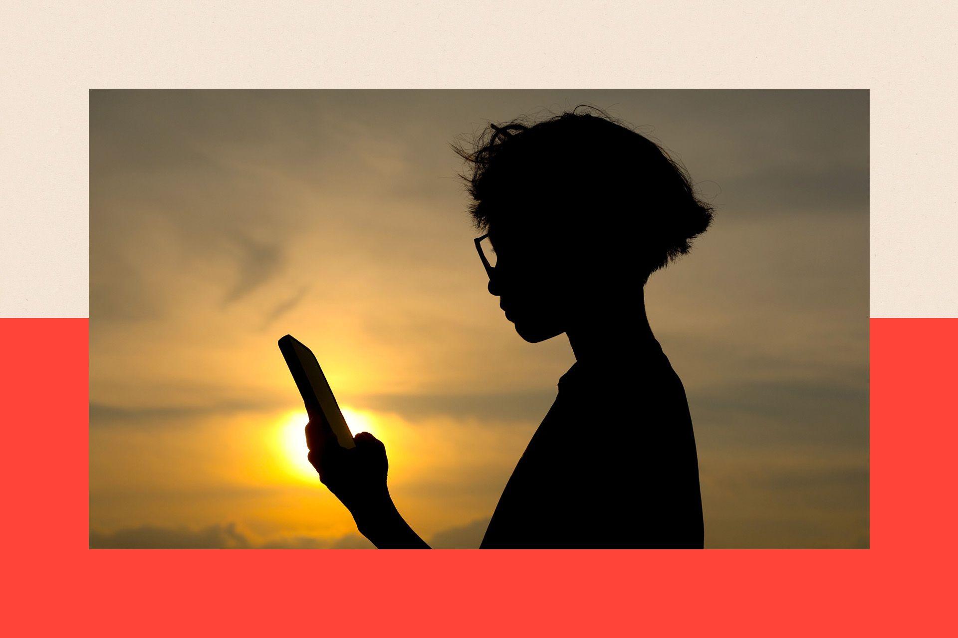 A silhouette of a child looking at his mobile phone. He has shoulder-length hair and is wearing glasses. The Sun is shining behind him.