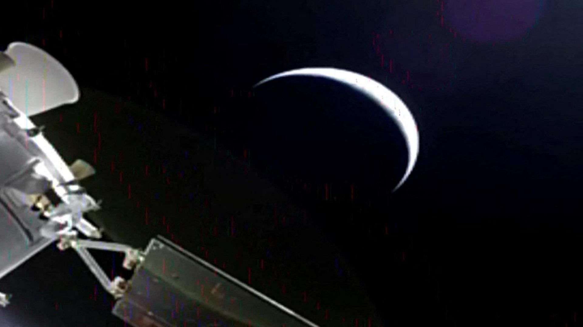 A slightly grainy image from Orion showing a planet - perhaps the moon, as a sliver with most of it in darkness, and part of Orion in the corner.