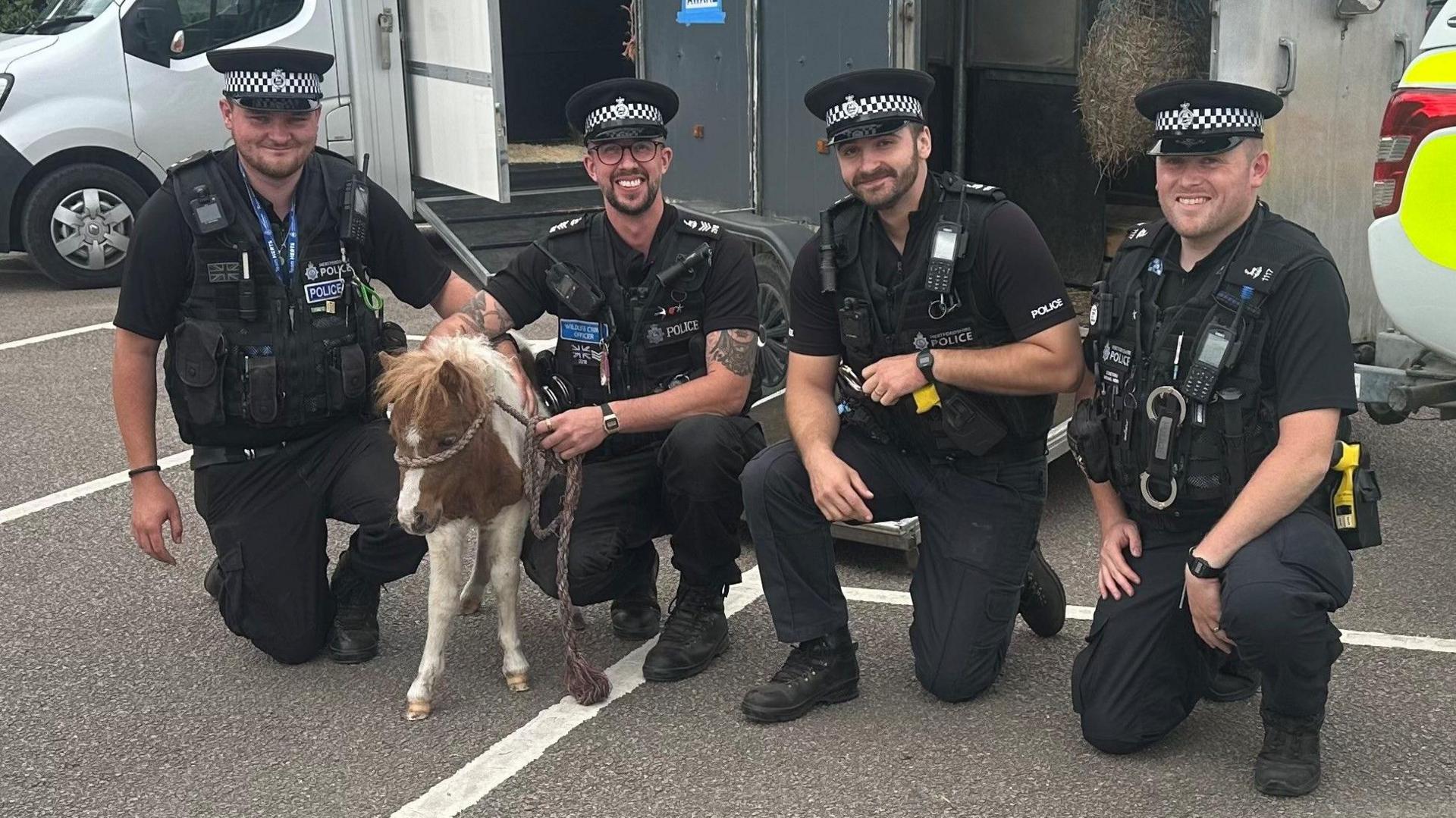 A group of 3 police officers pictured holding Lucy the foal. They are stood in front of a horse trailer and next to a police vehicle. There is a large van in the background too.