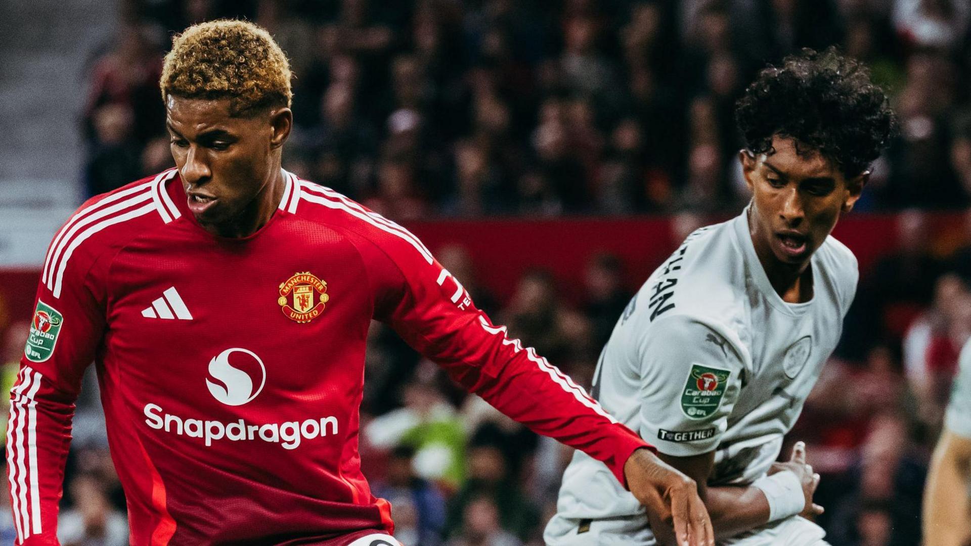 Marcus Rashford of Manchester United in action with Vimal Yoganathan of Barnsley during the Carabao Cup Third Round match between Manchester United and Barnsley at Old Trafford on September 17, 2024. Rashford is in United's signature red home kit while Vimal wears Barnsley's grey away kit. 